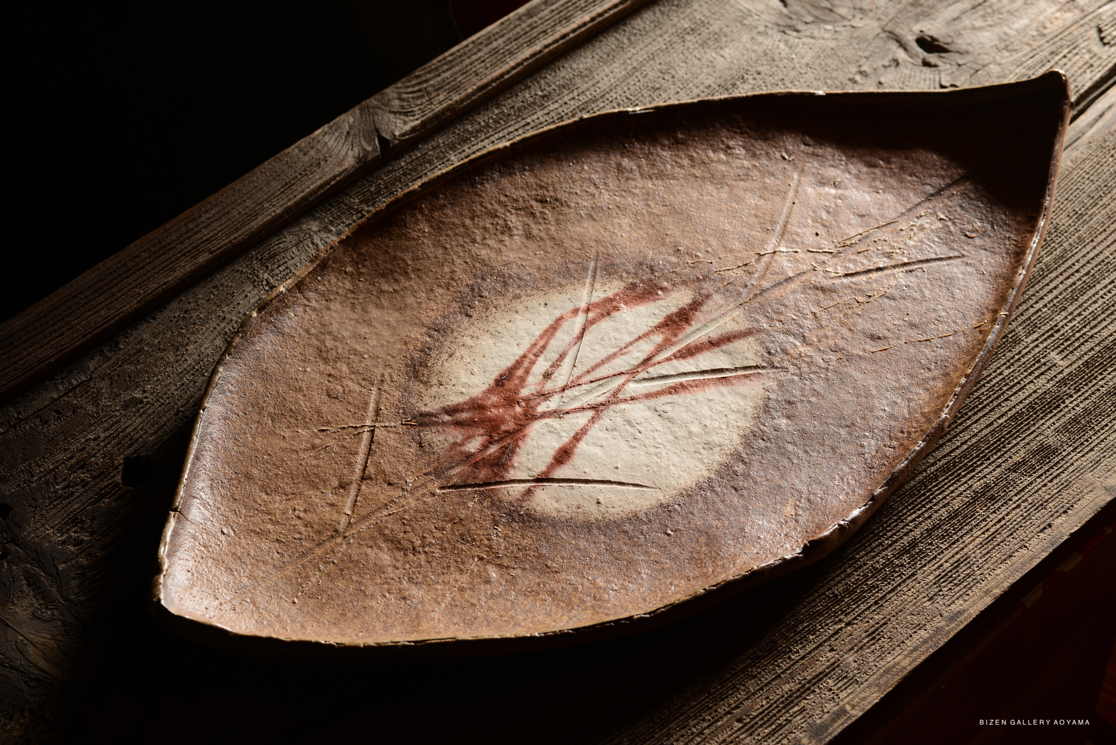 A decorative platter shaped like a leaf, featuring earthy tones and a subtle design, placed on a wooden surface.