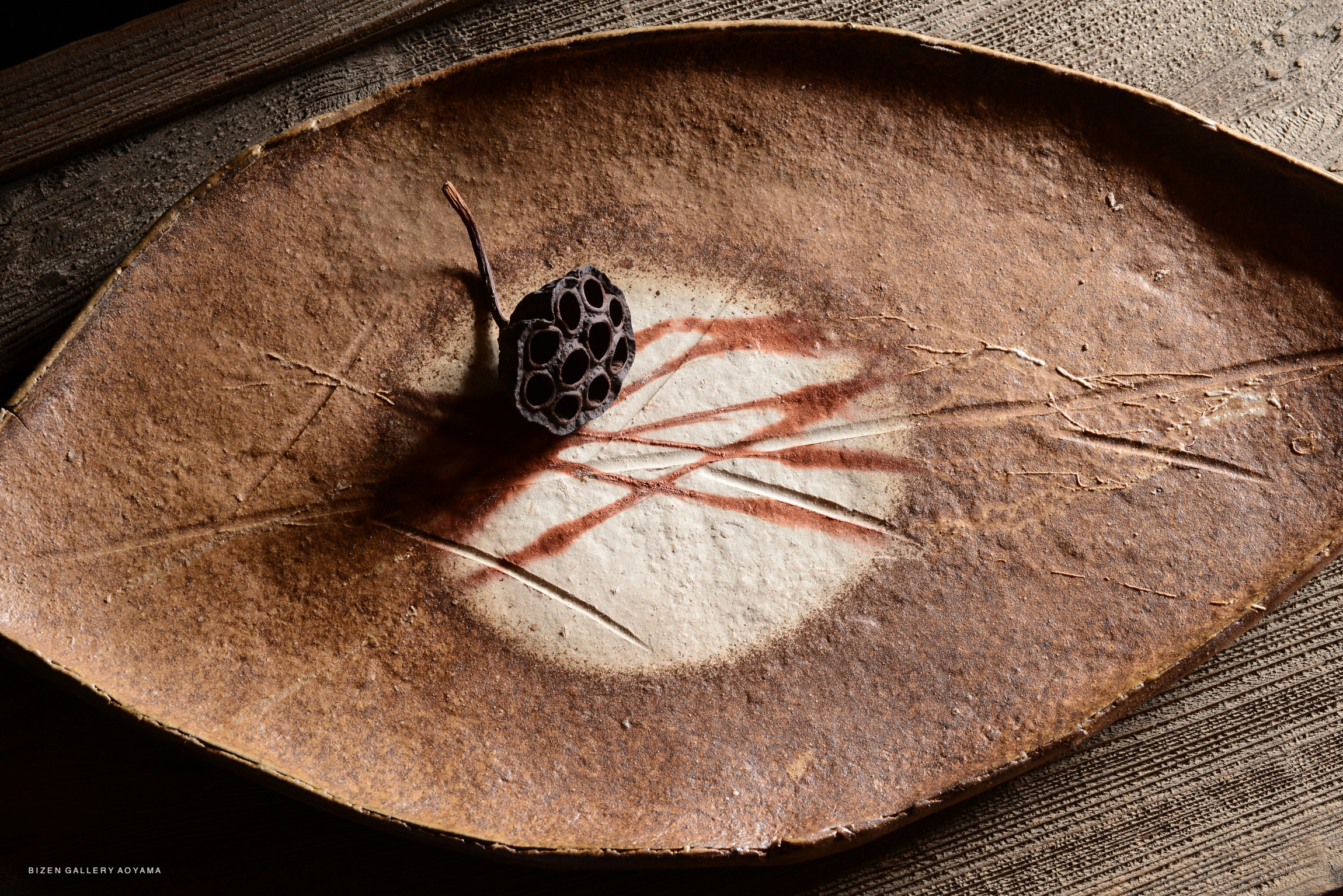 A leaf-shaped platter with a brown, textured surface and a small ornamental lotus pod placed in the center, showcasing artistic details.
