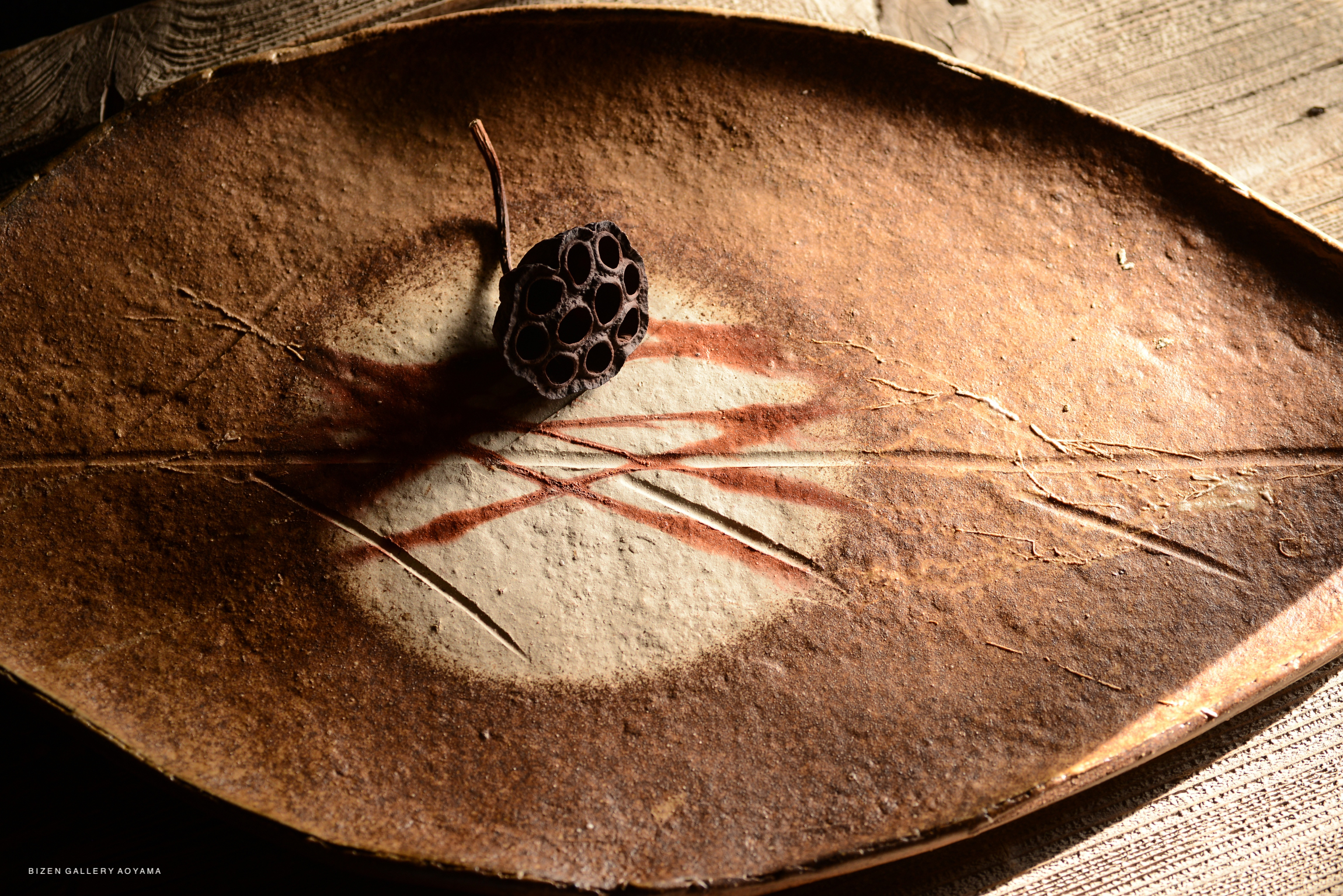 A leaf-shaped platter with a decorative lotus pod placed on top, featuring earthy tones and textures.