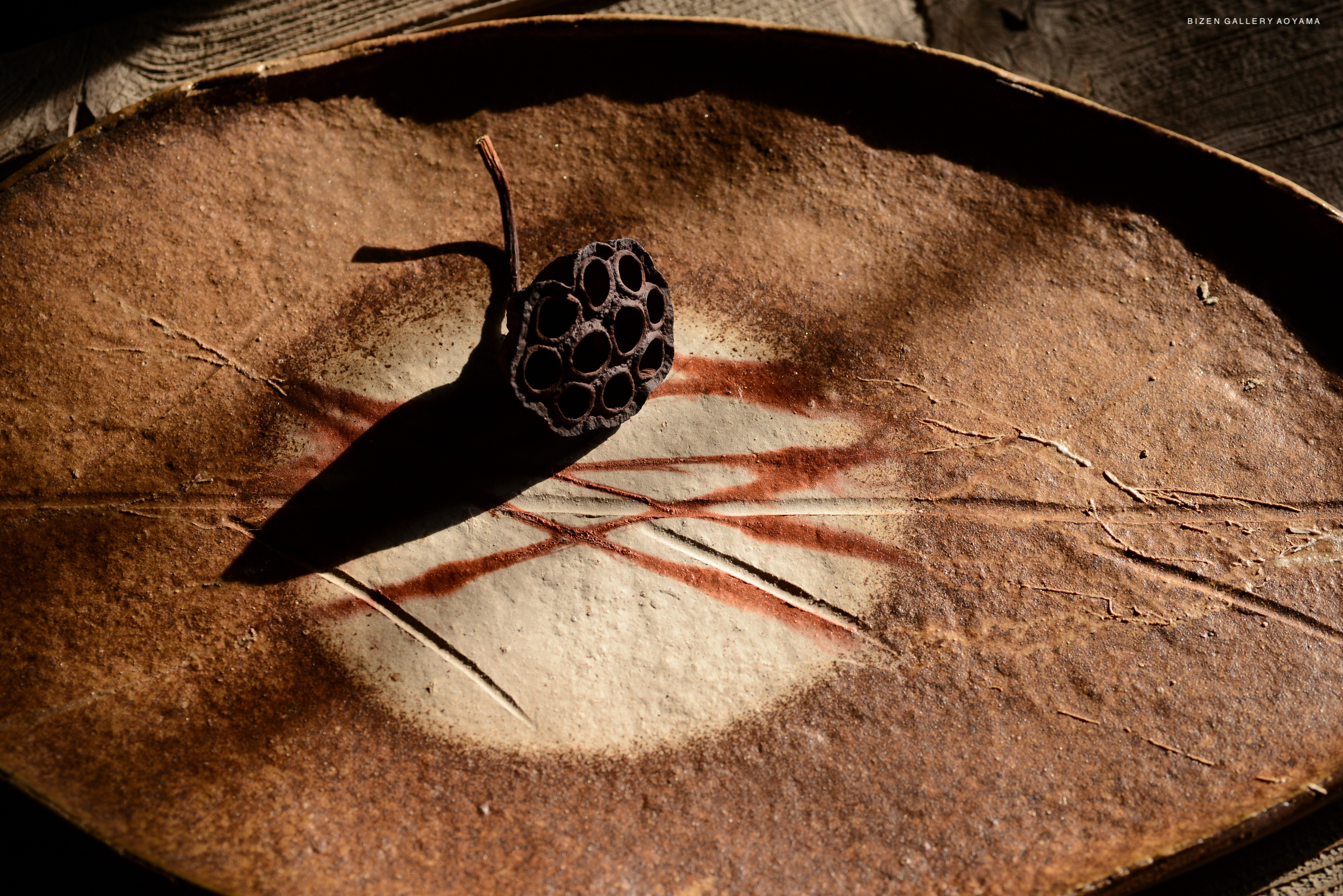A close-up of a leaf-shaped ceramic platter with a dark seed pod placed on it, featuring intricate textures and a natural finish.