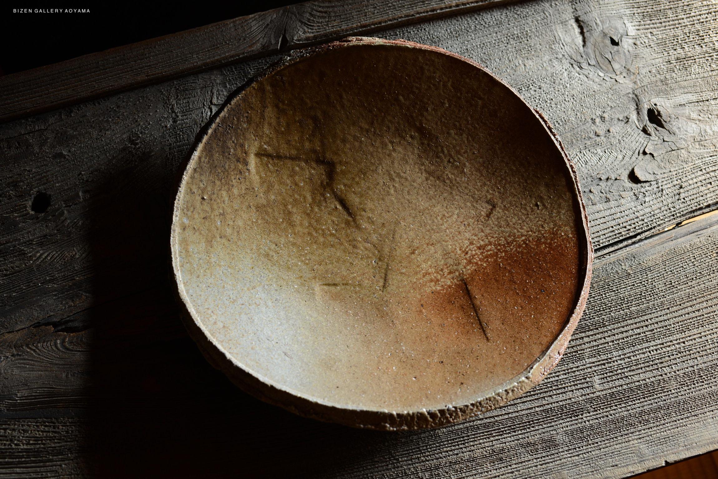 A Bizen tatakizara plate with a textured surface and natural earthy tones, placed on a wooden surface.