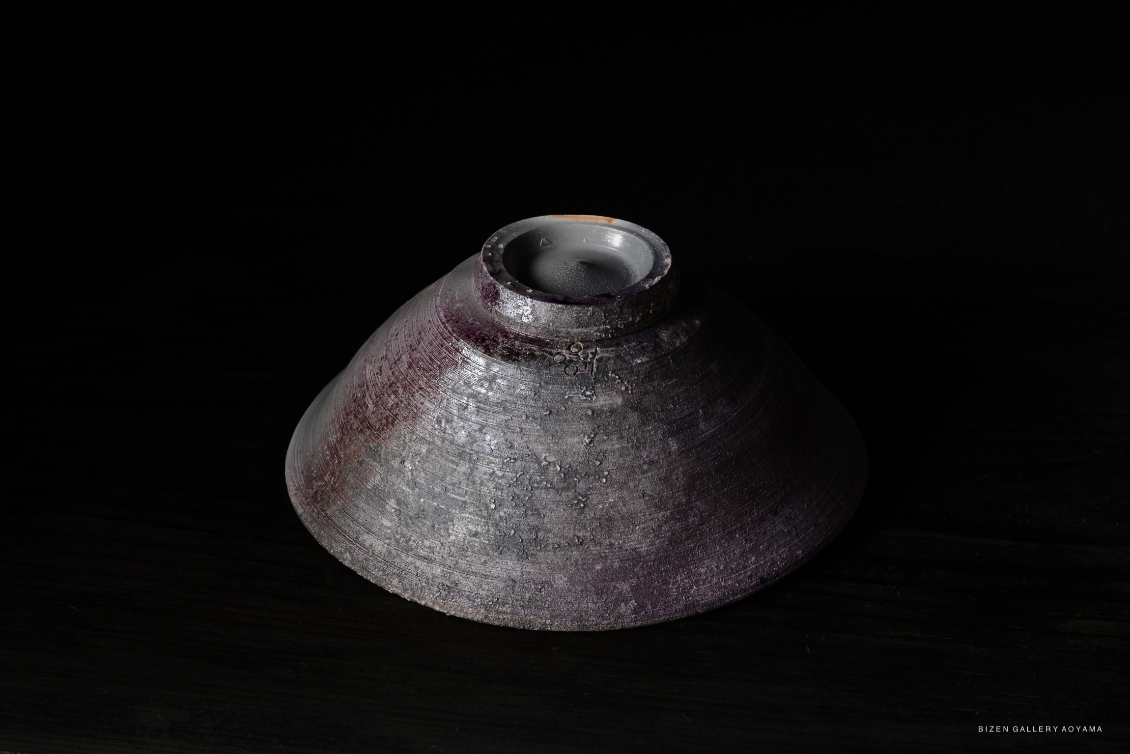 A unique ceramic bowl with a textured surface and a slight purple hue, displayed on a dark background.