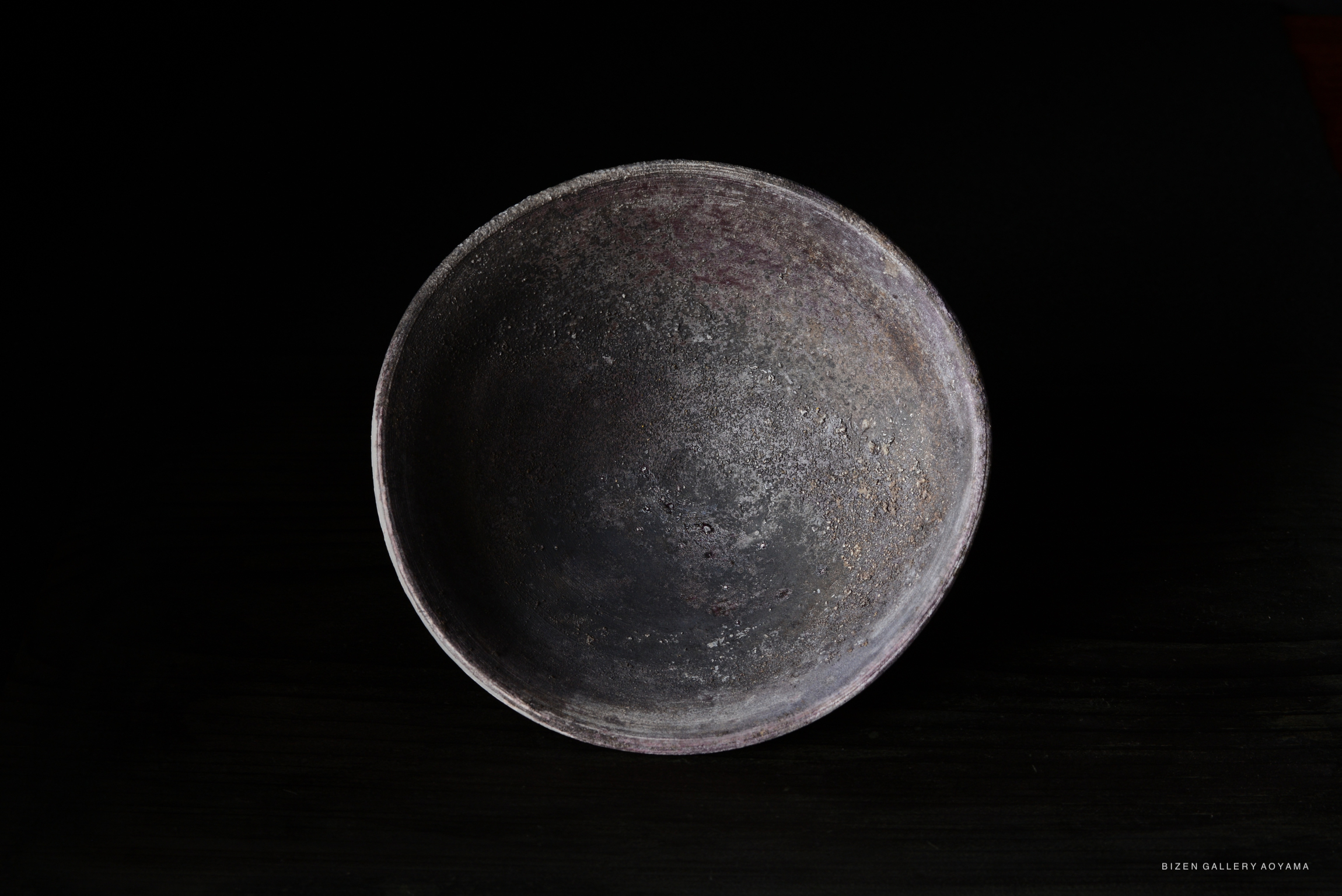 A top-down view of a textured, rustic ceramic bowl with a dark interior against a black background.