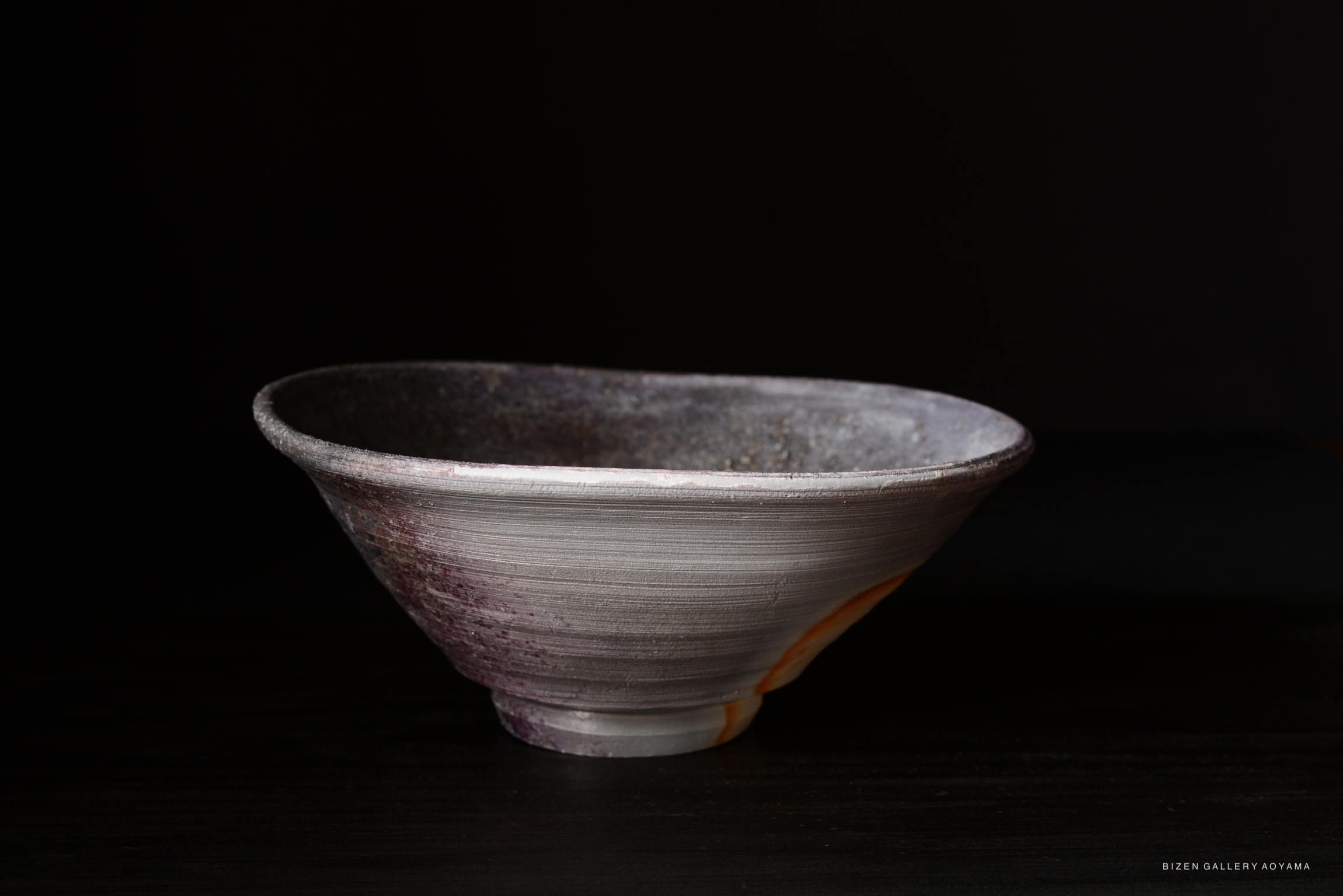 A handcrafted Bizen pottery bowl with a wide, flared lip, featuring a textured, earthy surface with subtle colors.