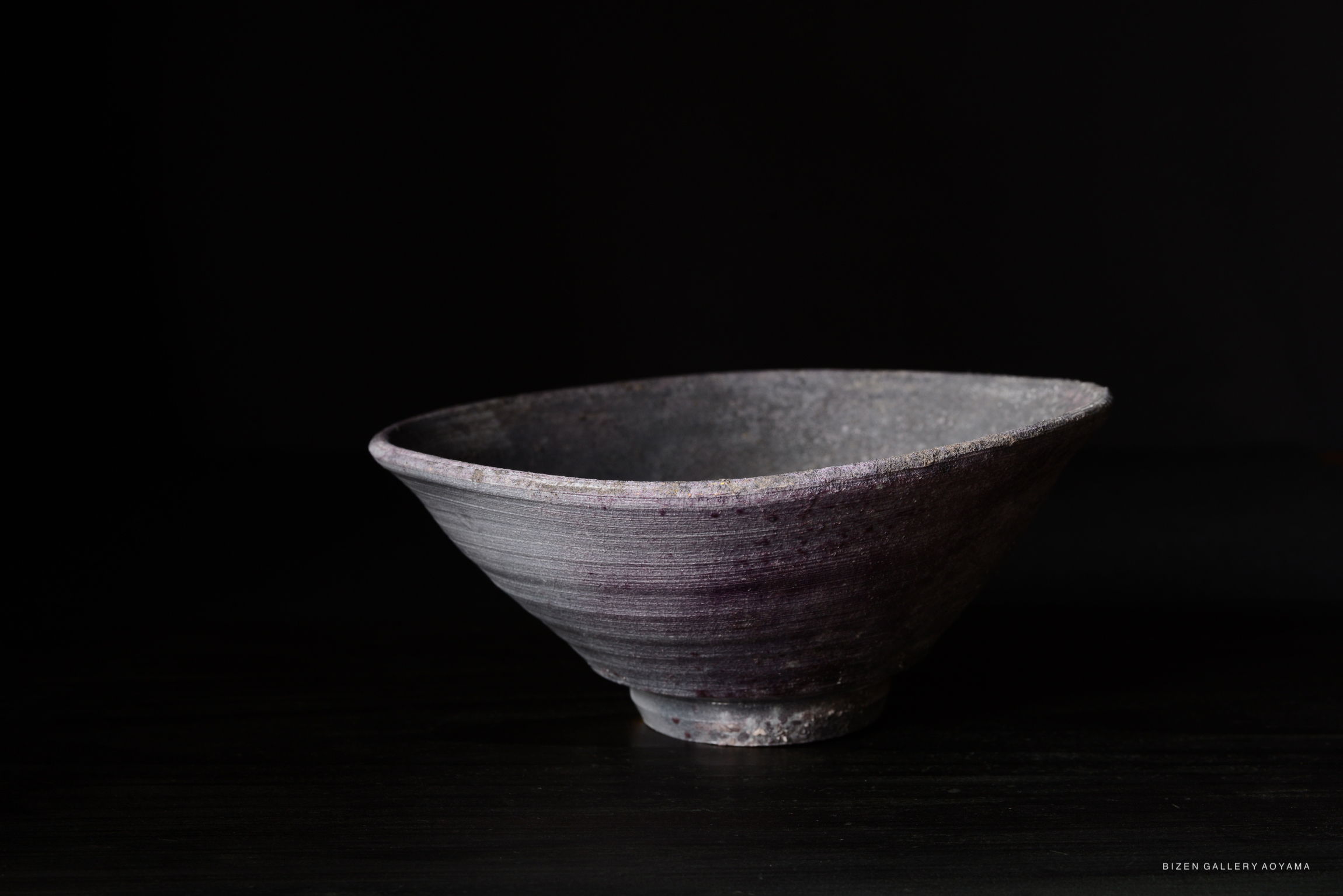 A handcrafted ceramic bowl with a square shape and subtle purple tones, set against a black background.