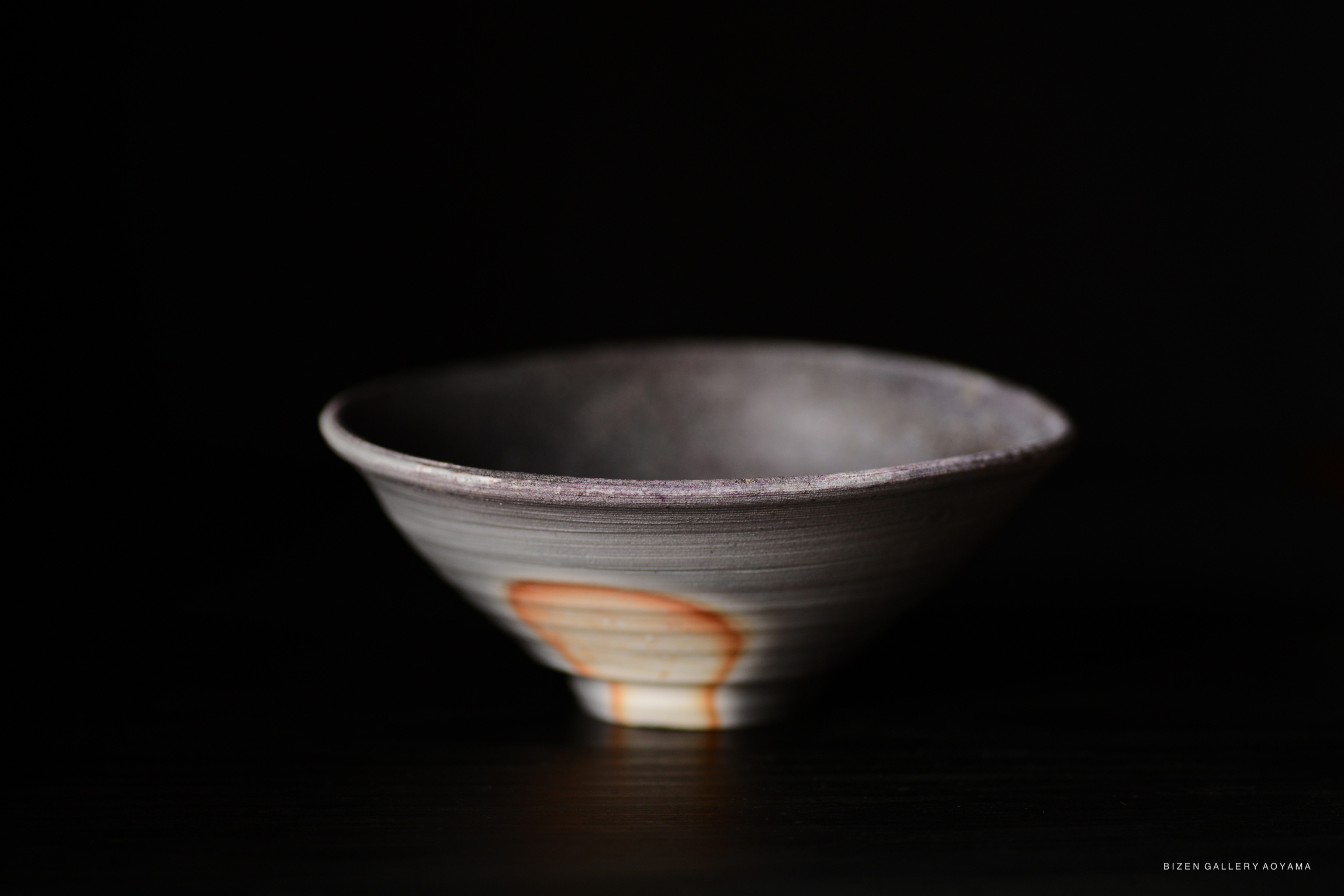 A close-up image of a handmade ceramic bowl with a textured surface and a unique glimmering design on the side, set against a dark background.