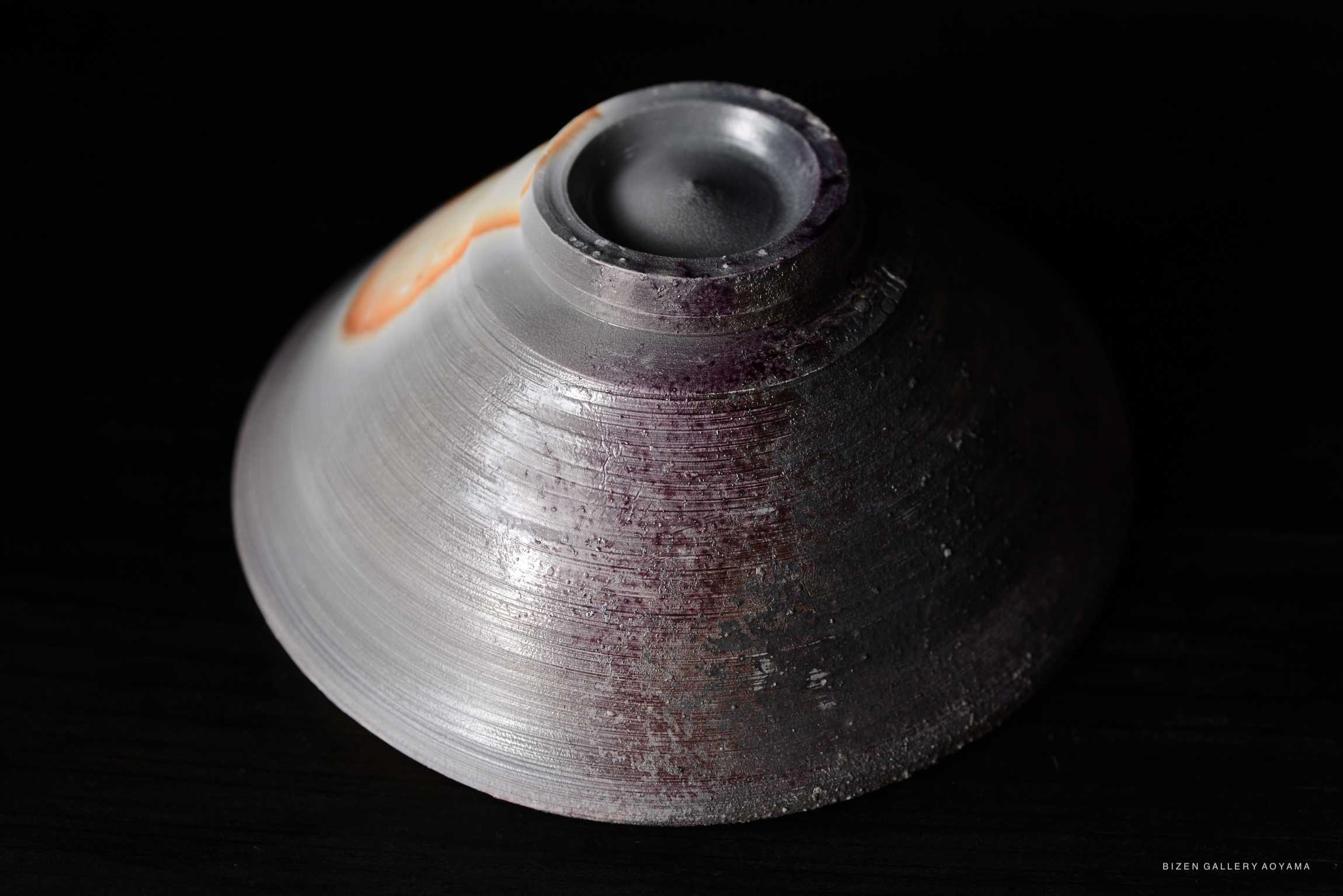 Close-up view of a ceramic bowl with a matte surface featuring subtle purple and orange hues, placed on a dark background.