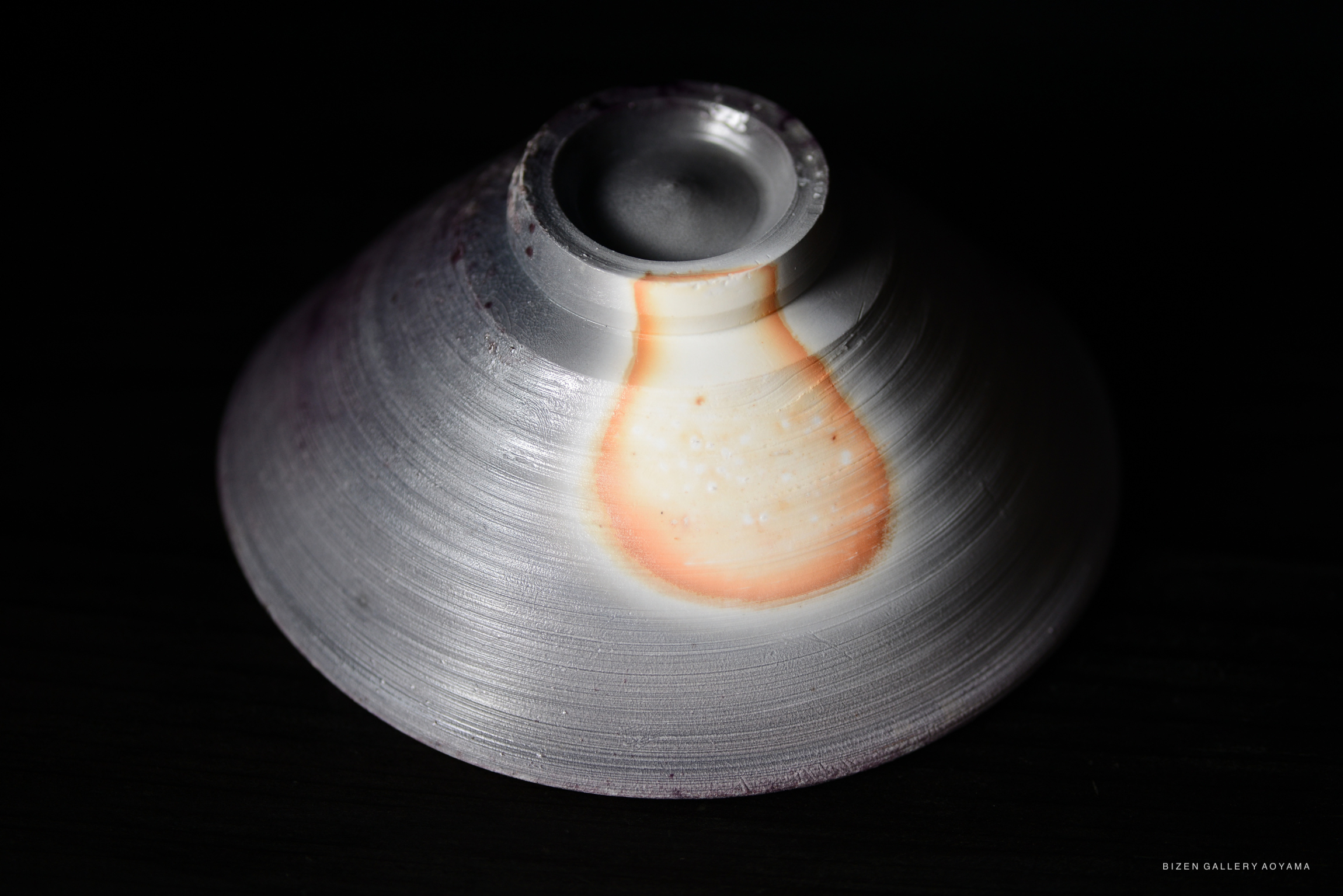 Close-up image of a beautifully crafted ceramic bowl with a glossy finish, featuring an orange and white color pattern against a dark background.