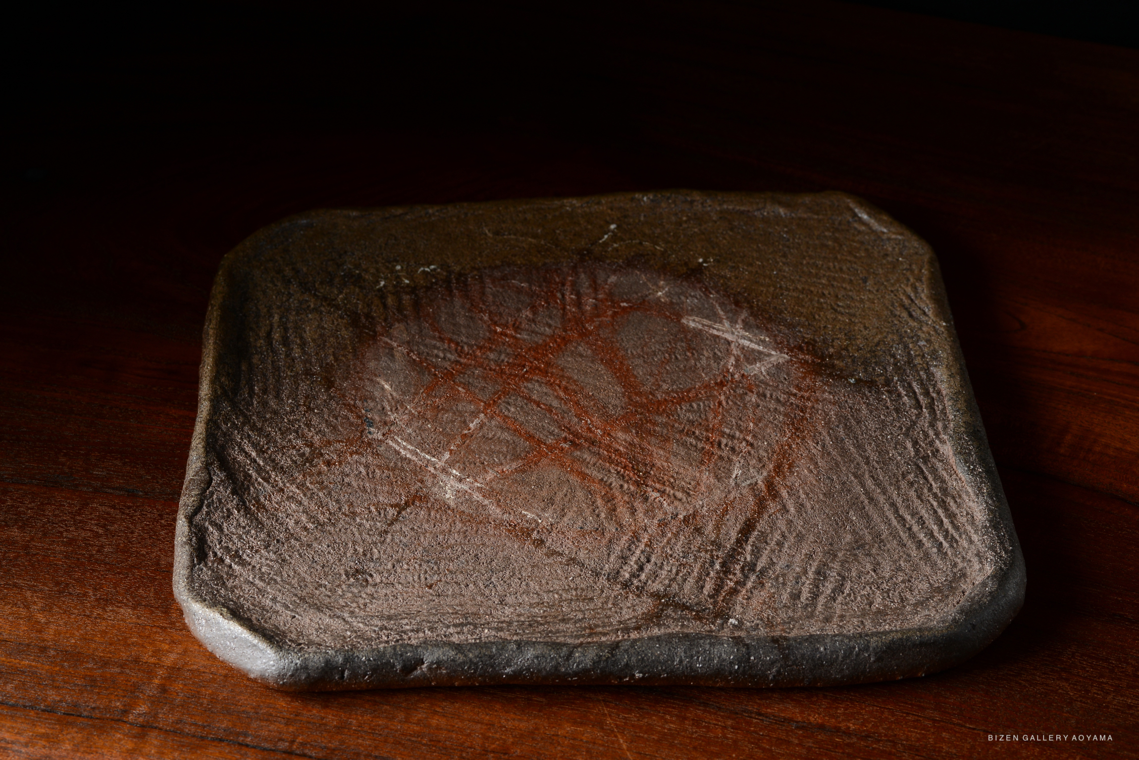 A textured clay plate with distinctive markings on its surface, displayed on a wooden table.