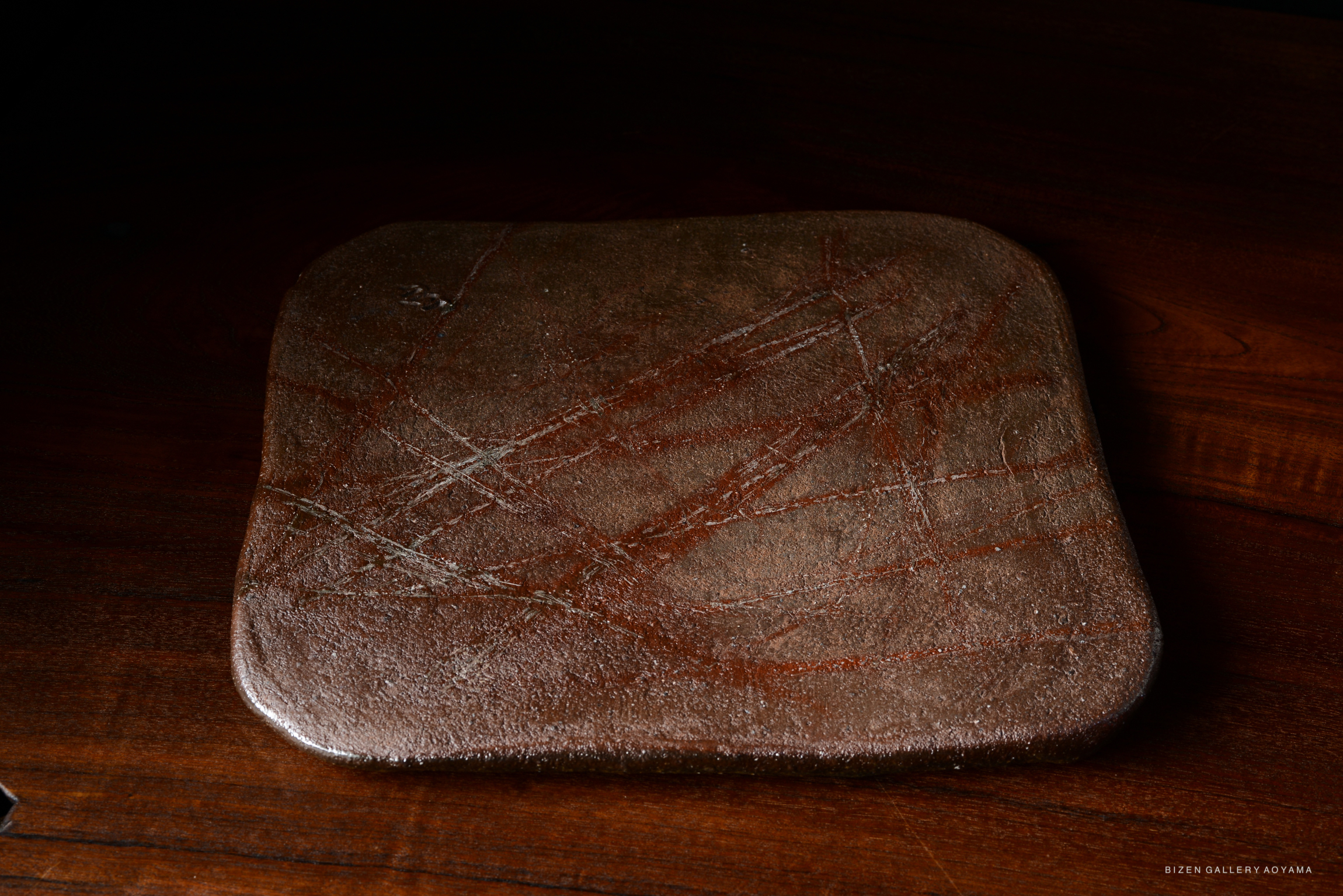 A textured, brown serving platter with scratches and markings, placed on a wooden surface.