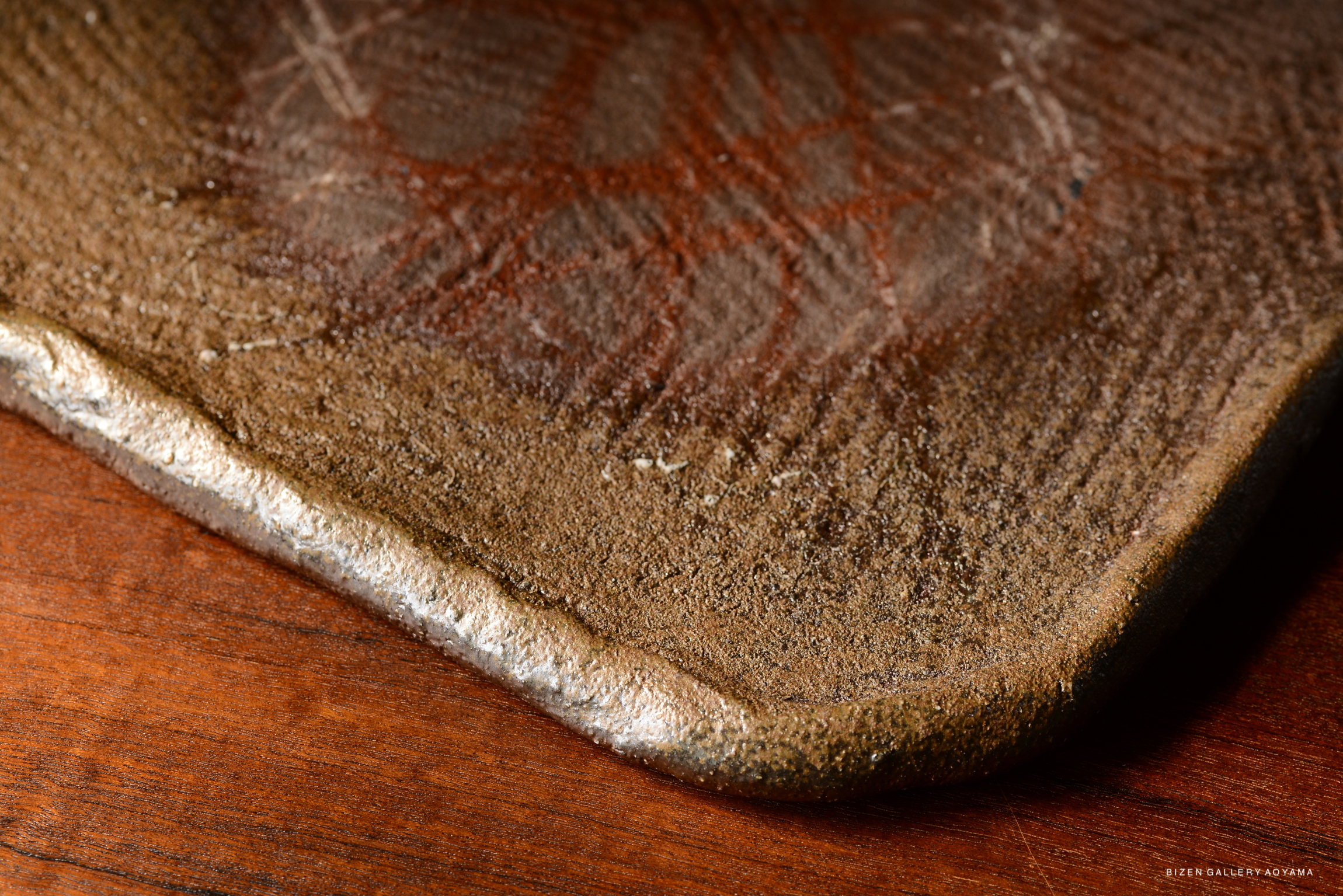 Close-up view of a textured ceramic surface with a metallic edge resting on a wooden table.