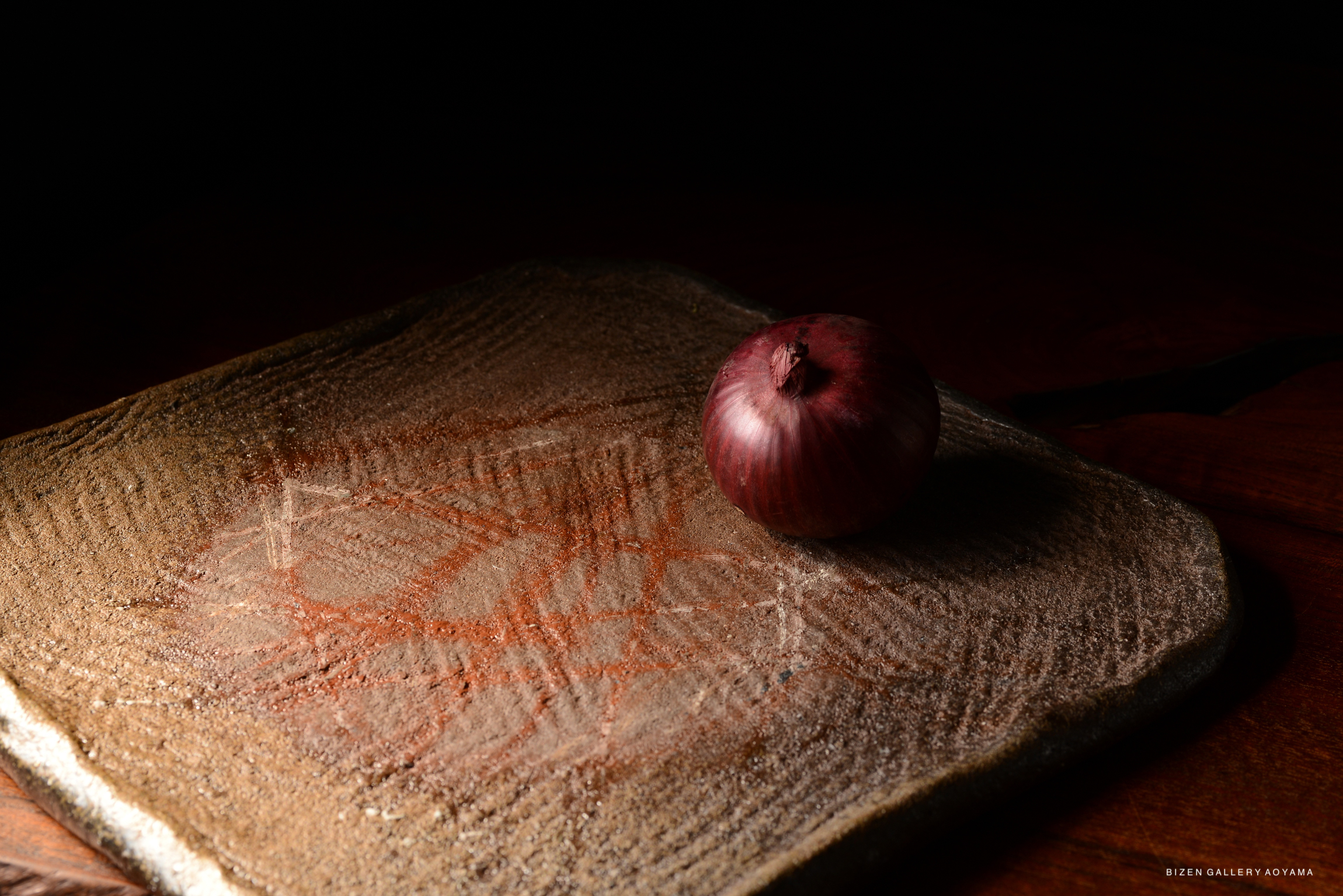 A close-up image of a red onion resting on a textured stone surface with faint patterns, set against a dark background.