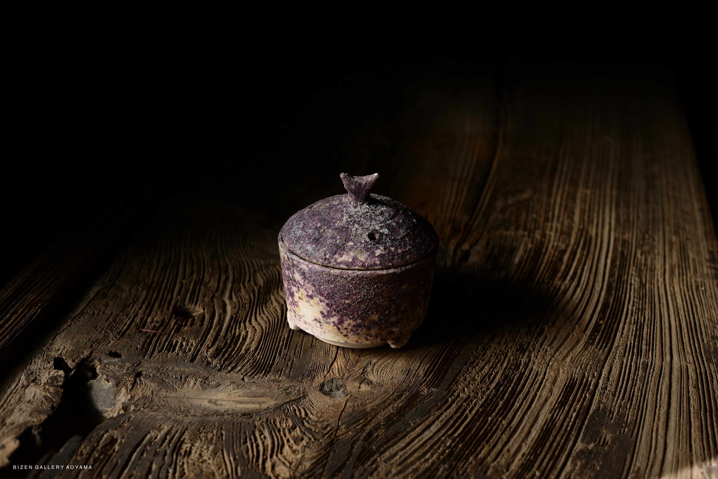 A purple ceramic container with a lid, resting on a wooden table with a textured surface.