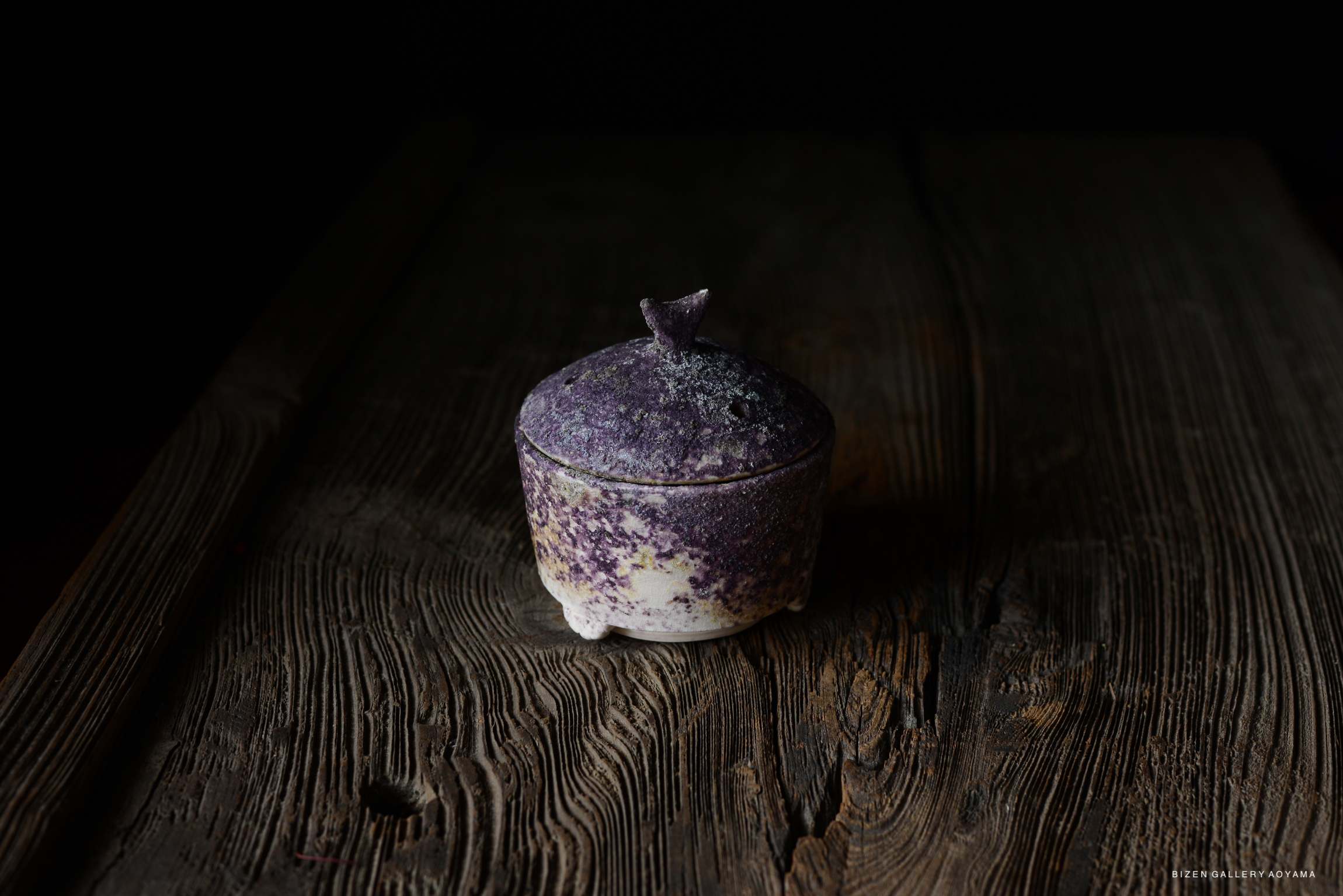 A purple and white ceramic container with a lid, placed on a wooden surface, illuminated by soft light.
