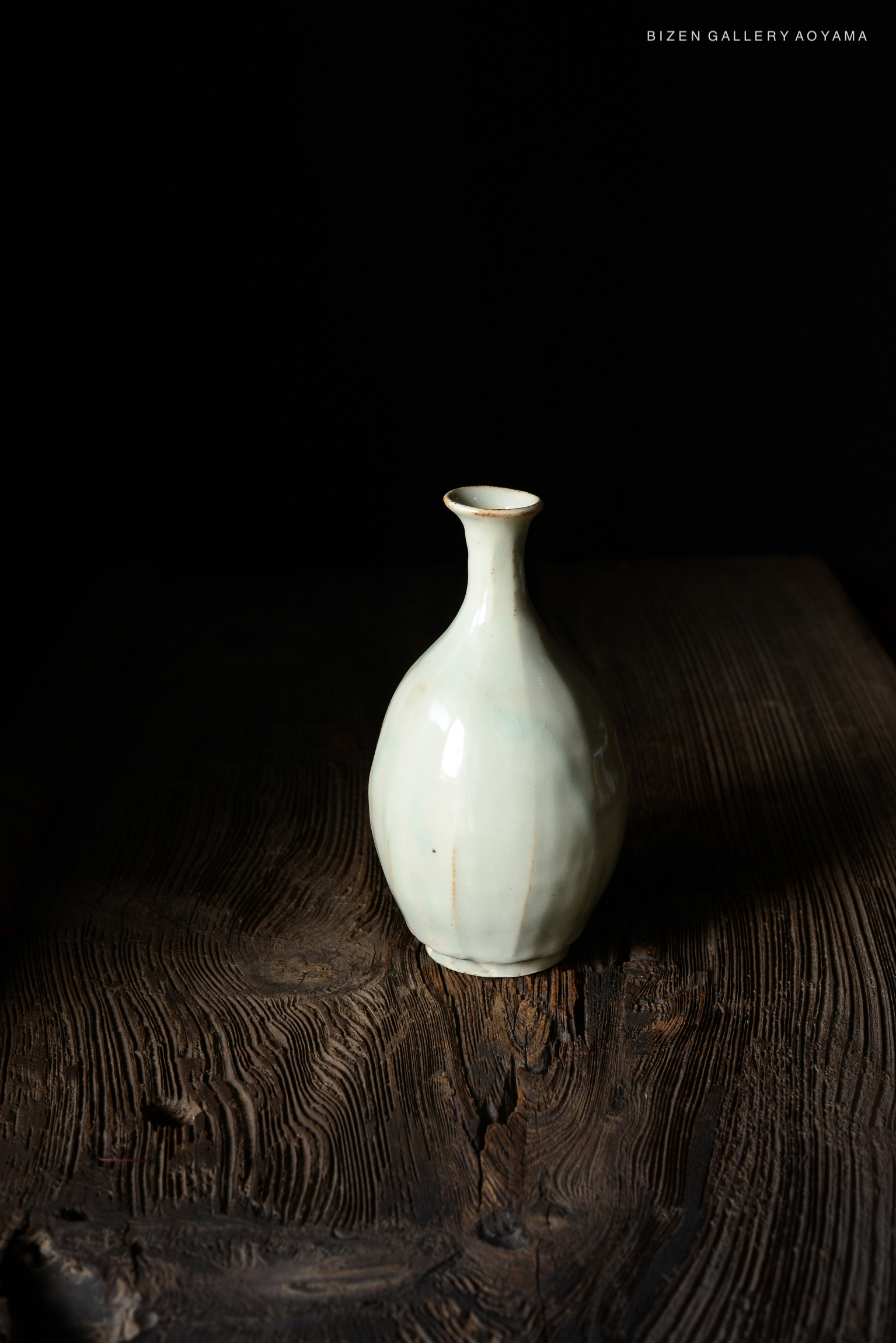 A pale ceramic vase with a round body and a narrow neck, positioned on a dark wooden surface.