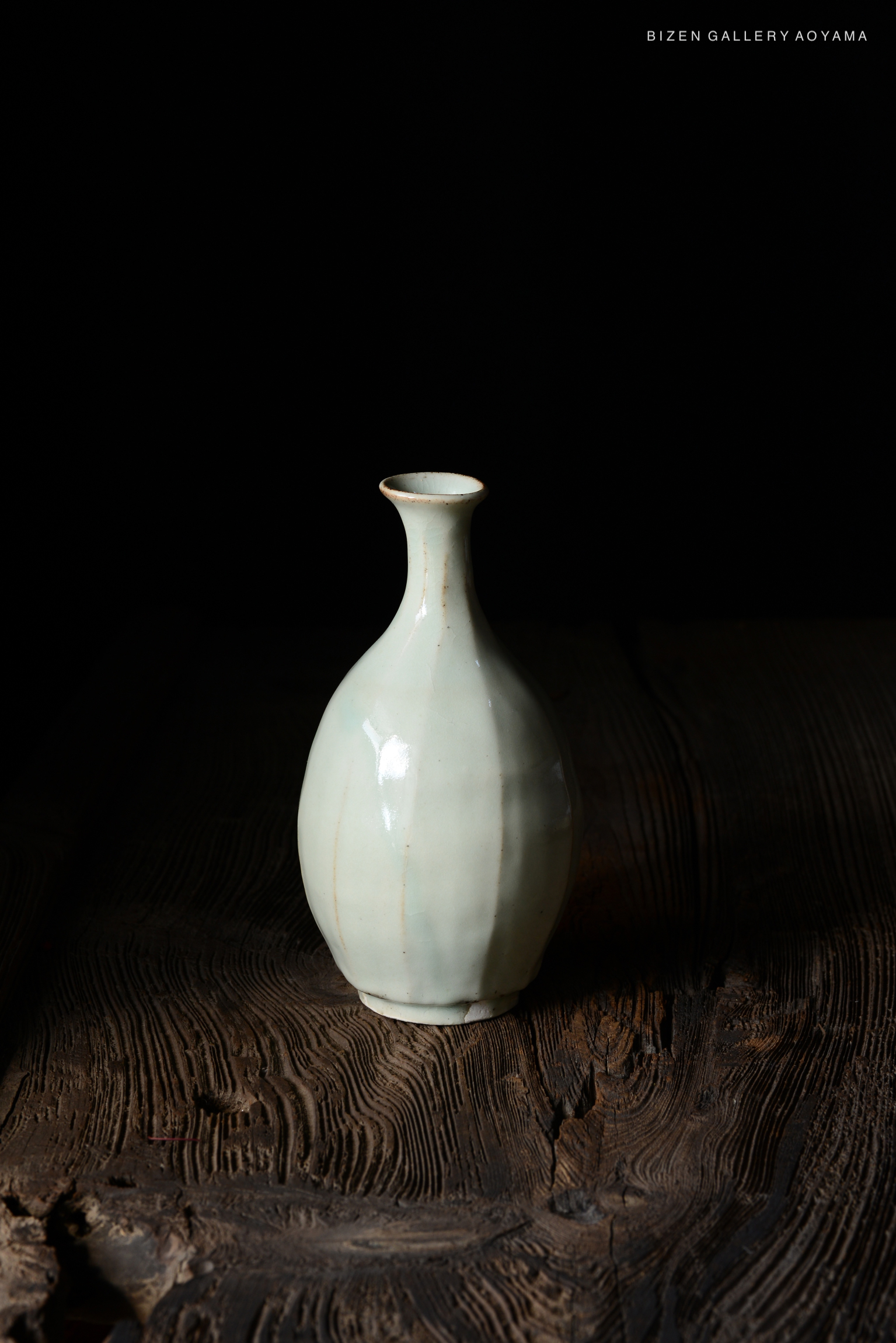 A pale ceramic vase with a slender neck and rounded body, placed on a textured wooden surface.