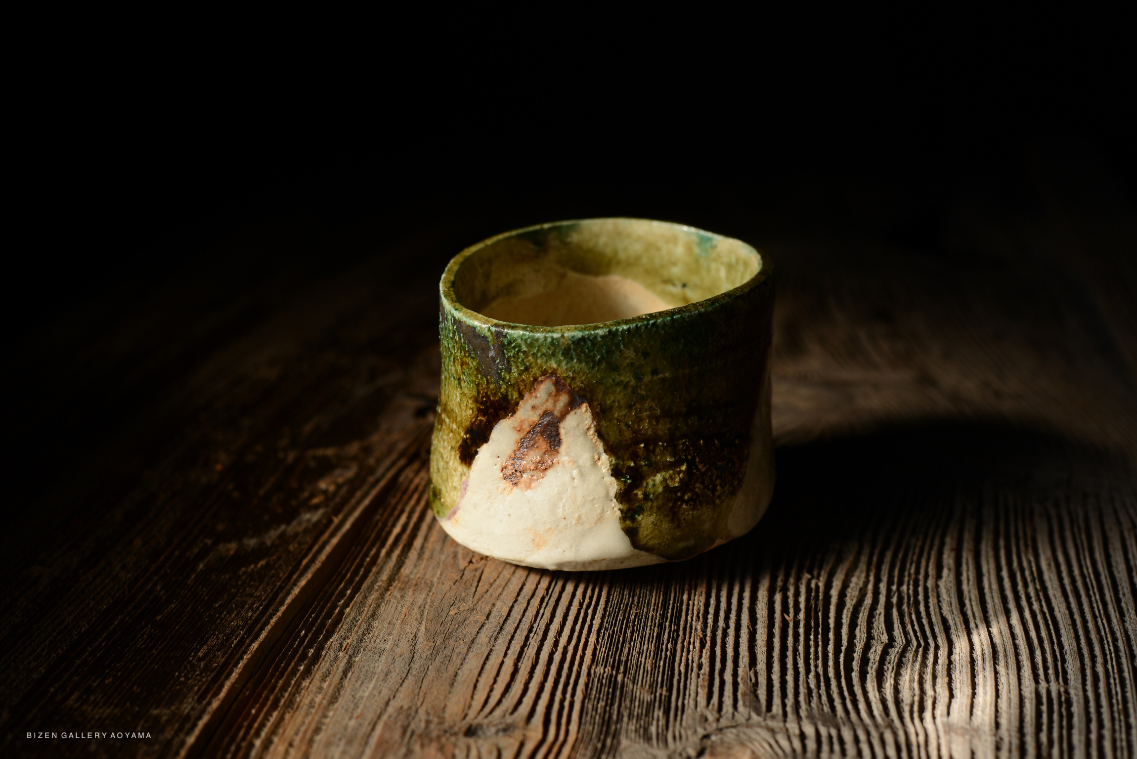 A handcrafted ceramic cup with a textured green and white glaze, placed on a wooden surface.