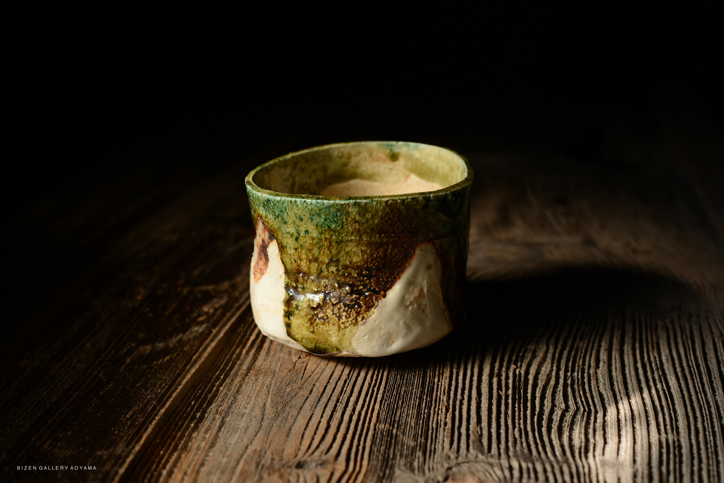 Close-up of a handcrafted ceramic cup with a green and earthy glaze, placed on a rustic wooden surface.