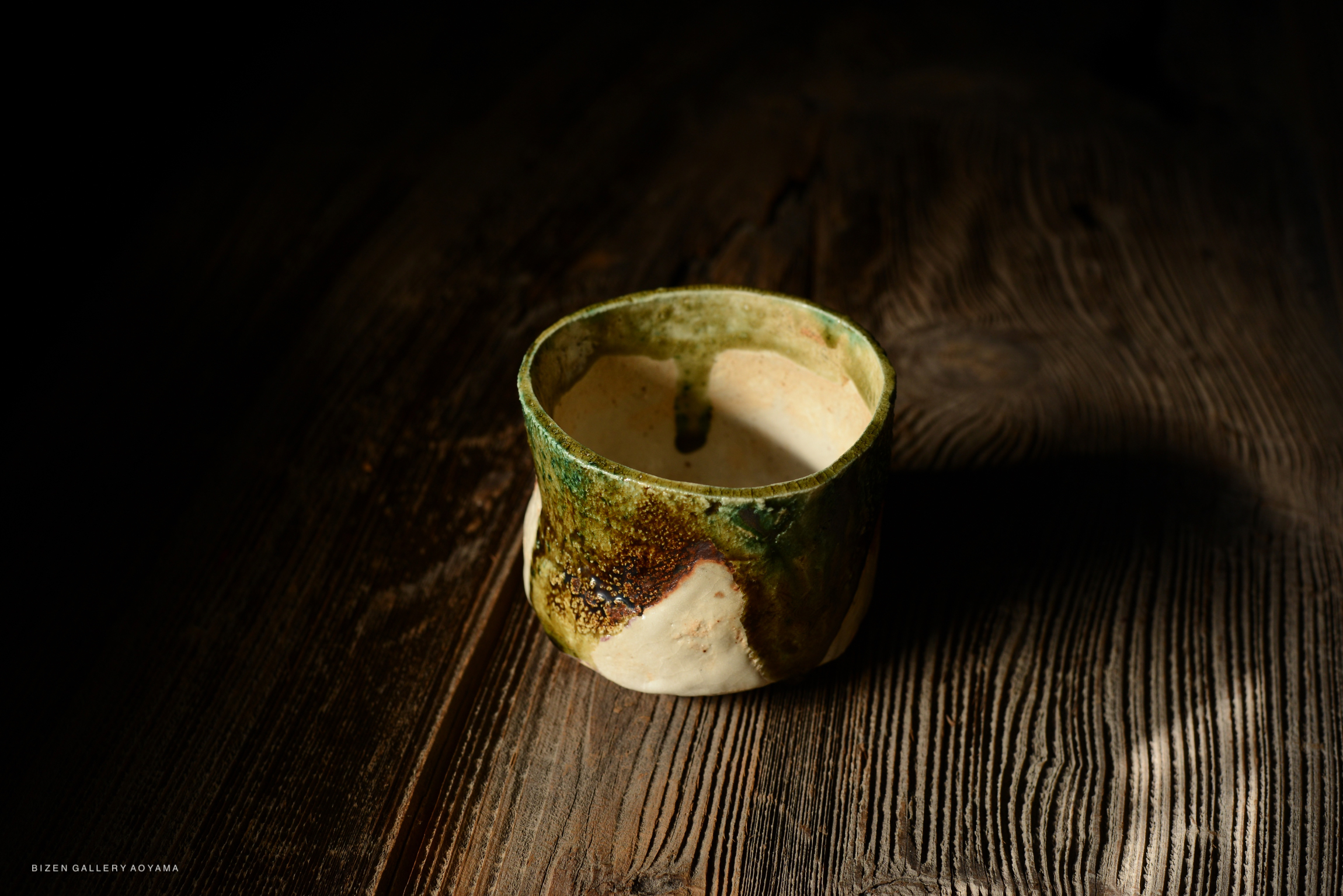 Artistic ceramic bowl with a textured surface and earthy colors, sitting on a wooden table.