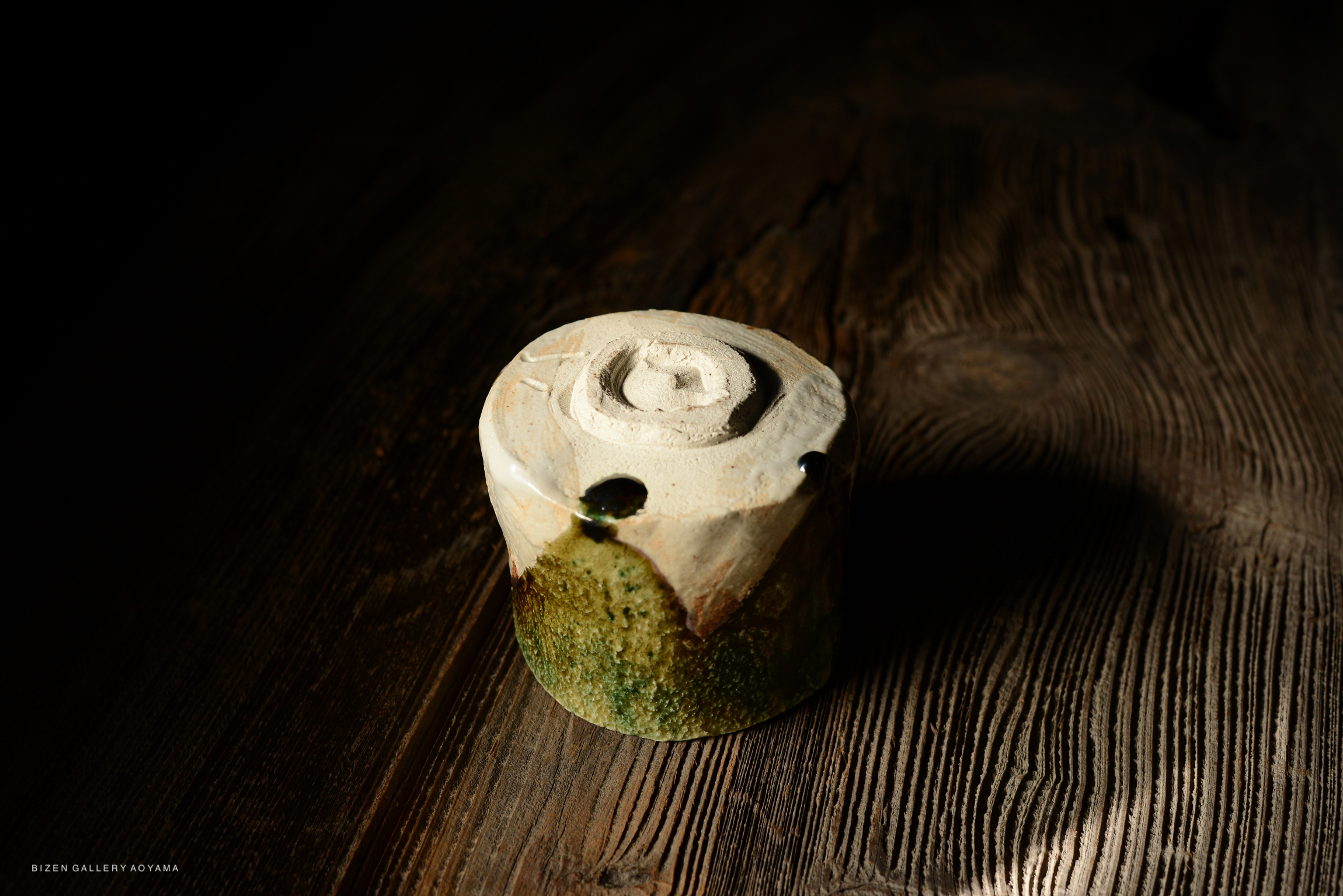 A close-up of a handmade ceramic piece with a textured surface, featuring a spiral design on top, placed on a rustic wooden table.