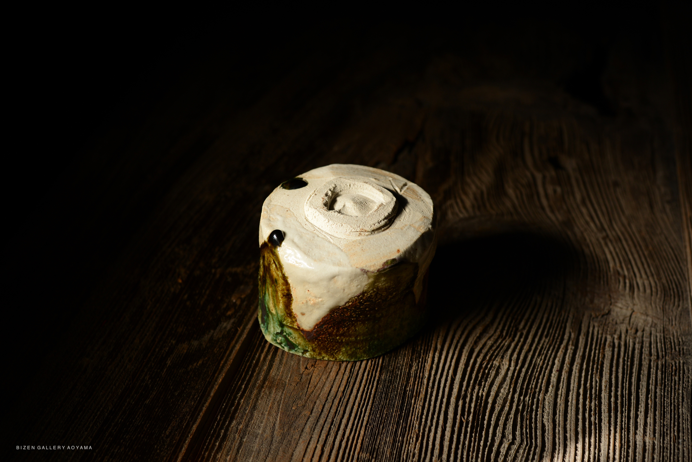 A close-up of a handcrafted ceramic pot with a textured glaze, resting on a wooden surface illuminated by soft light.