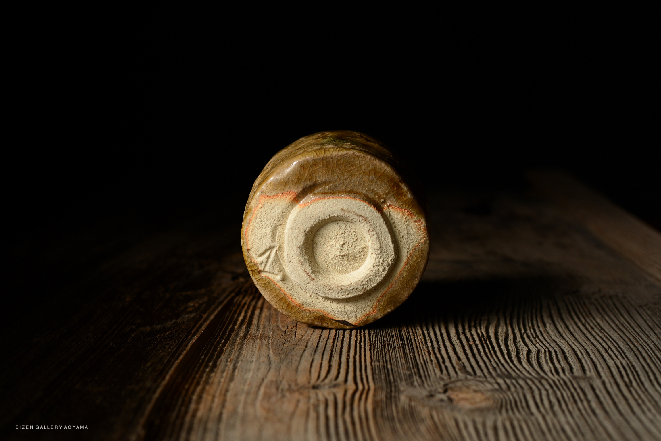 Close-up of the bottom of a pottery piece with a circular base on a wooden surface.