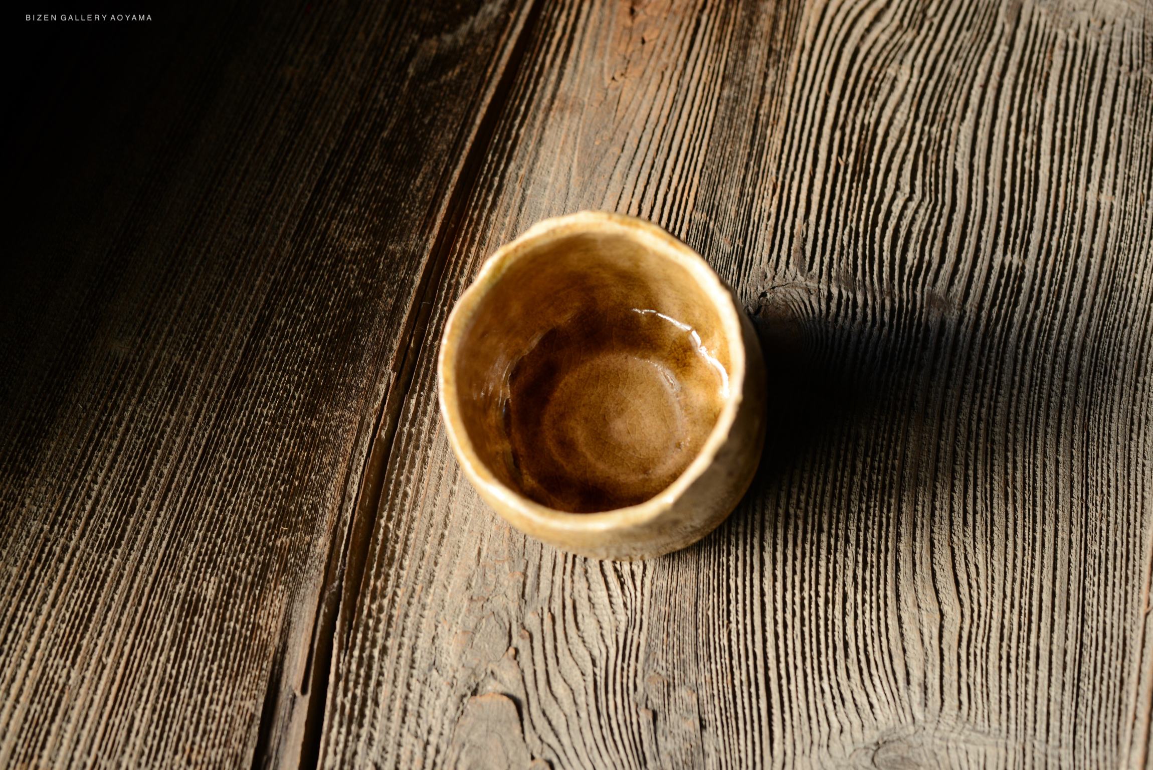 A close-up of a handcrafted ceramic bowl resting on a textured wooden surface.