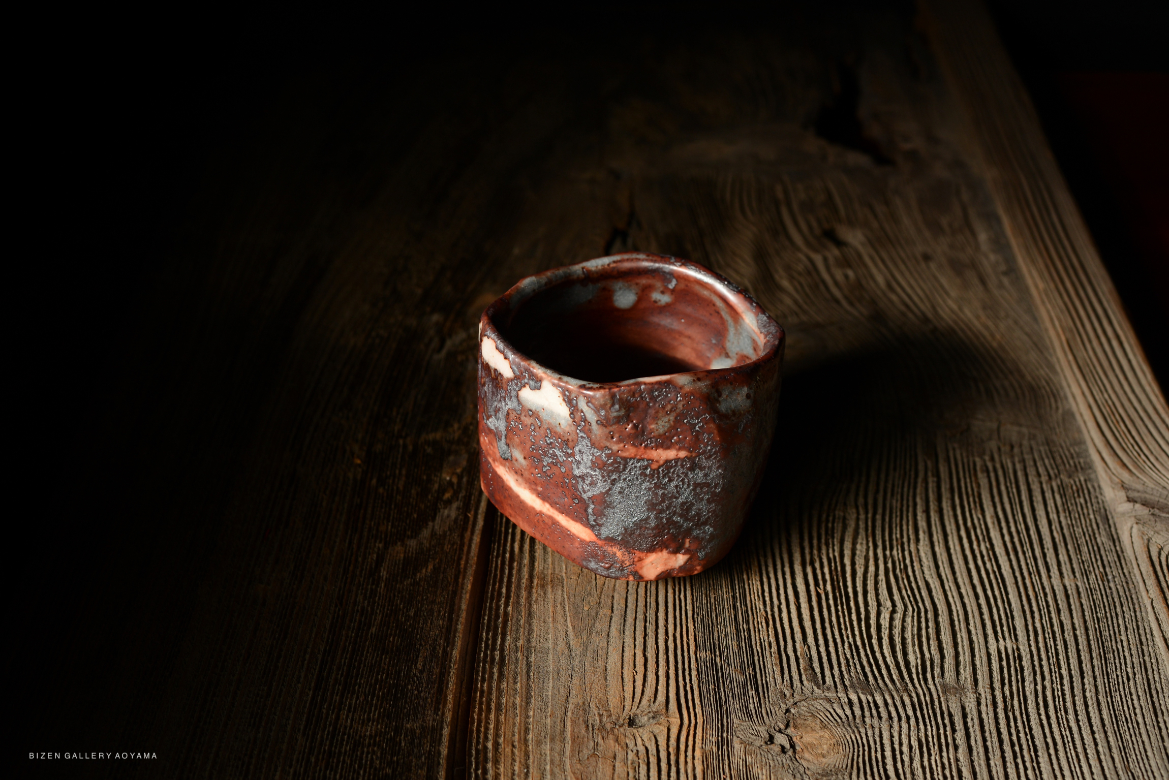 Close-up of a textured ceramic cup with a natural, earthy color palette, placed on a wooden surface.