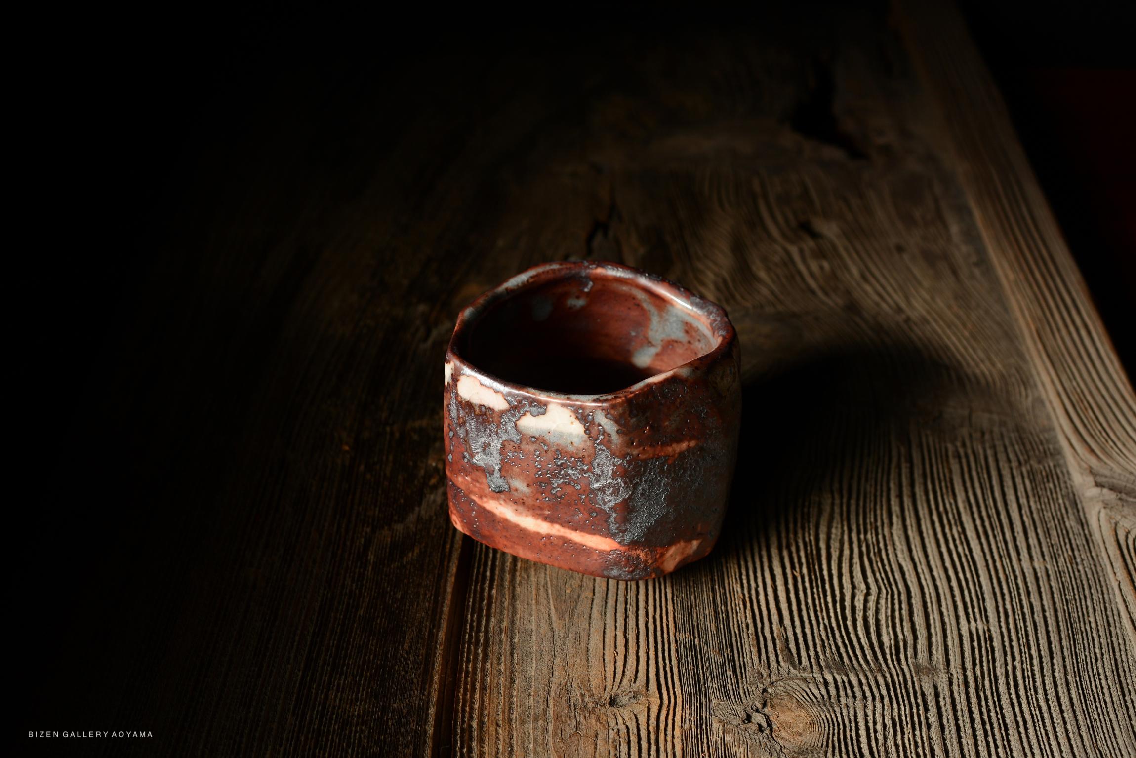 A handcrafted ceramic cup with a textured surface resting on a wooden table.