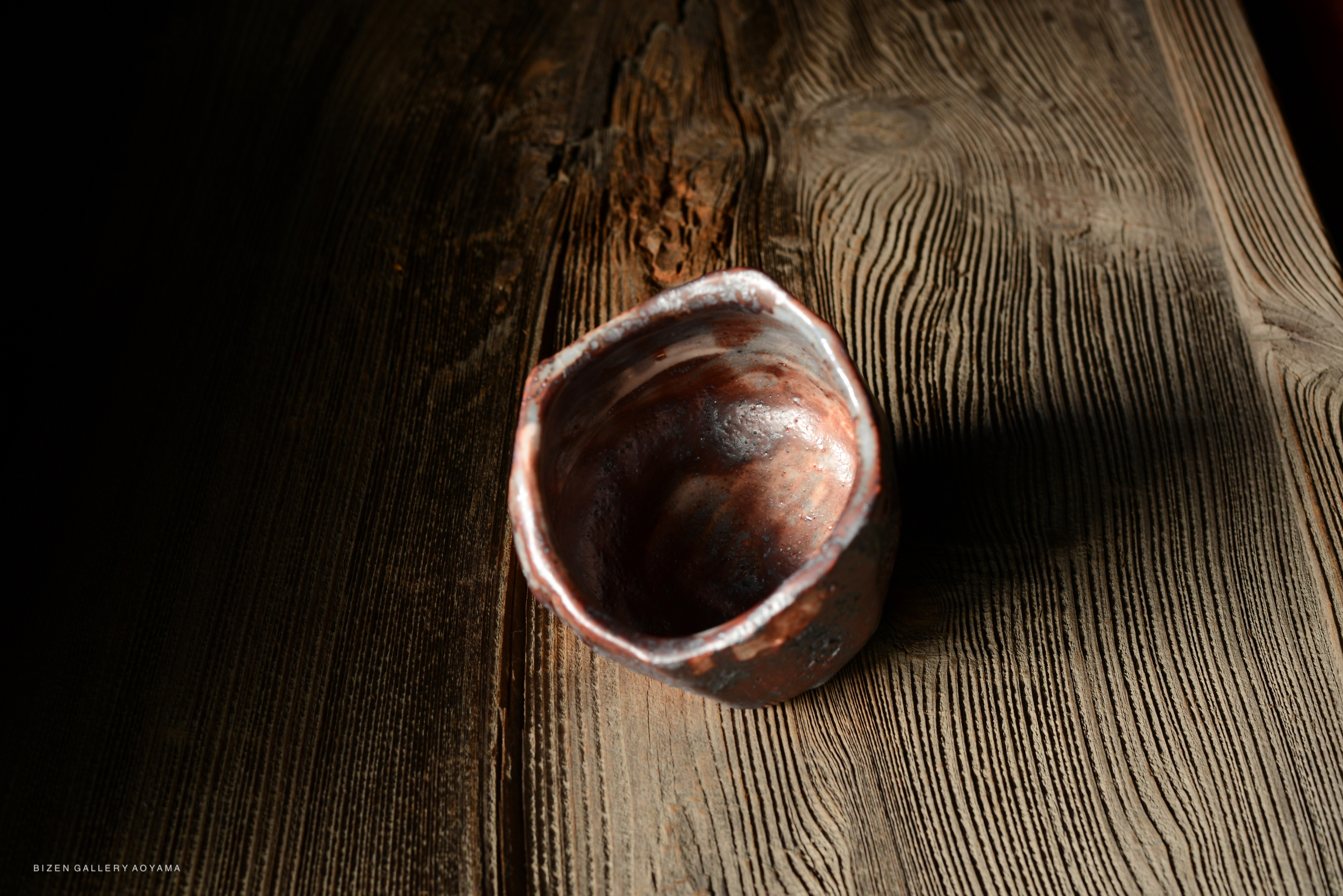 A close-up of a handcrafted, irregular-shaped ceramic bowl resting on a textured wooden surface, showcasing natural colors and a glossy finish.