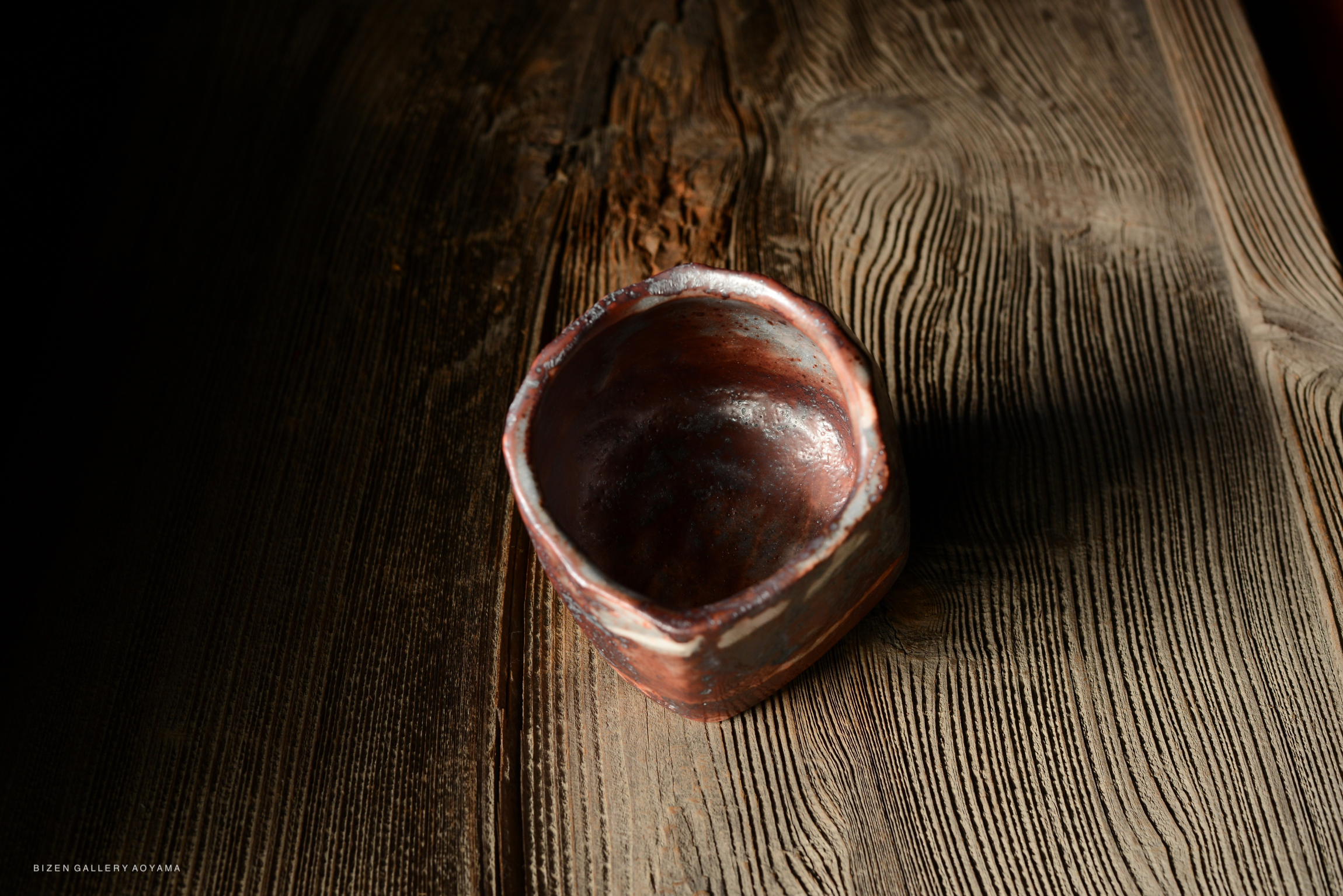 A close-up view of a rustic, handmade ceramic bowl resting on a textured wooden surface.