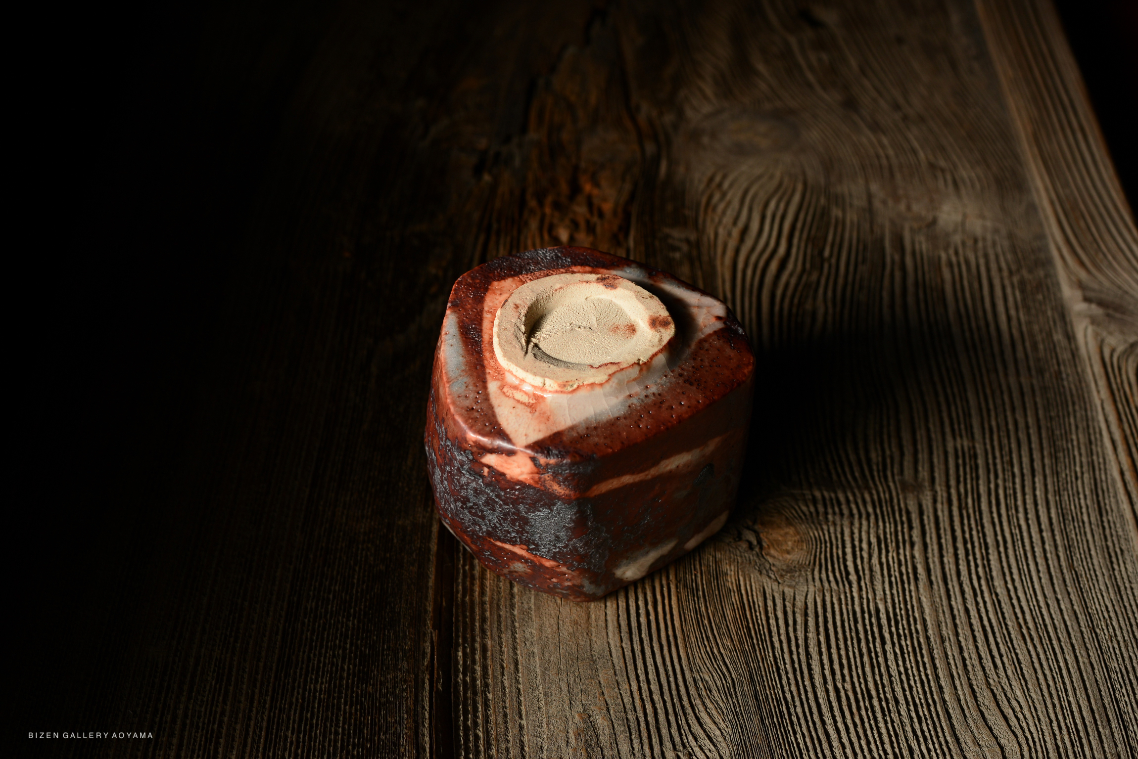 A top view of a uniquely shaped ceramic piece with a smooth, beige interior and a reddish-brown exterior, placed on a textured wooden surface.