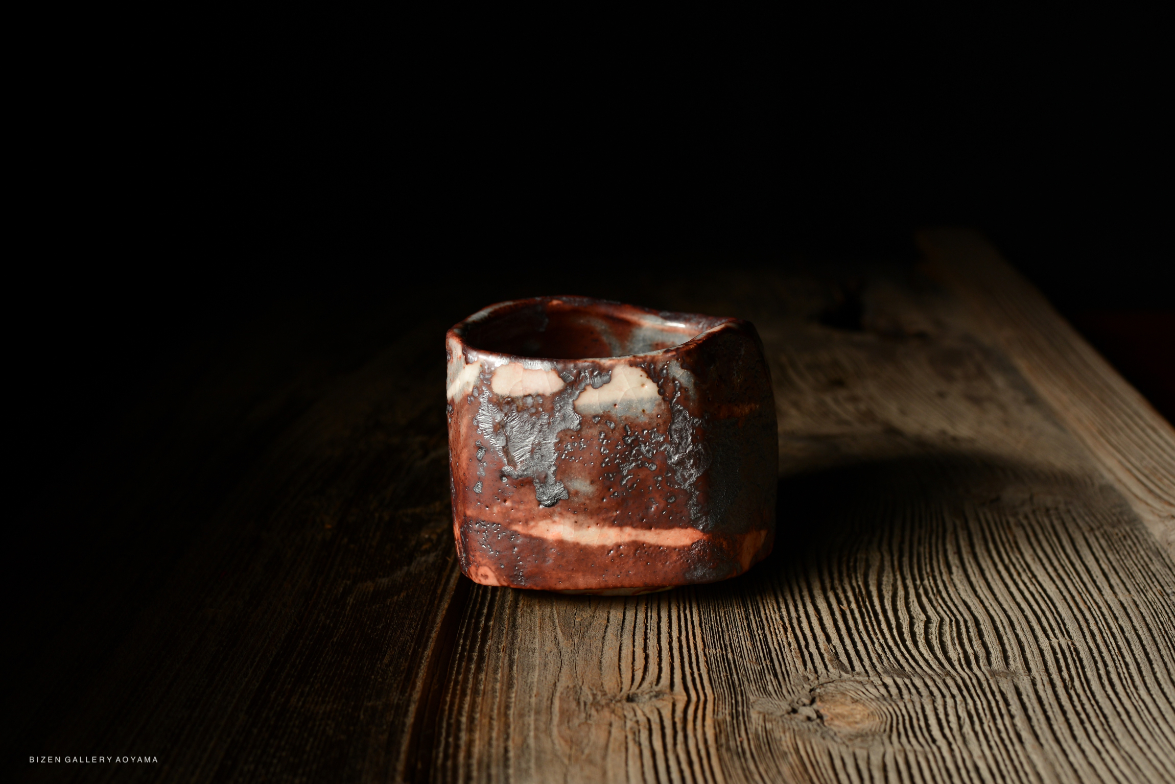 A close-up of a rustic ceramic cup on a wooden surface, showcasing its textured surface and earthy colors.