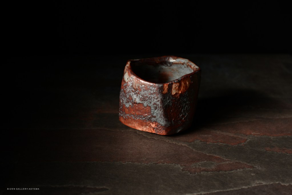 A unique, handcrafted ceramic bowl with a textured red and gray surface, displayed against a dark background.