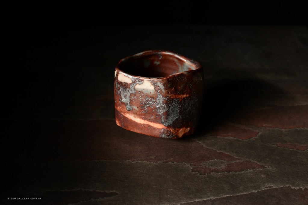 A ceramic tea bowl with a unique shape and textured surface, displayed against a dark background.