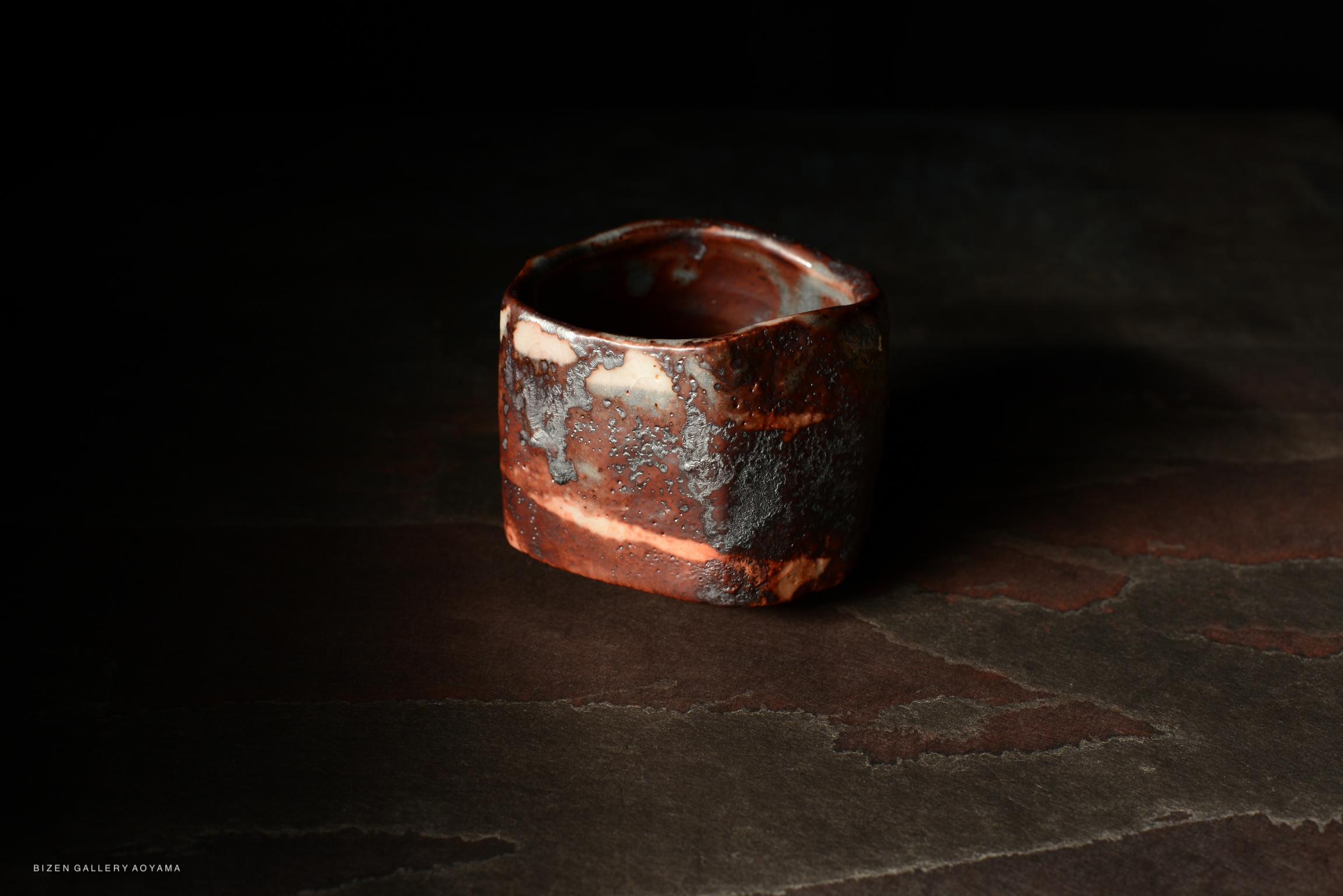 A close-up view of a Bizen pottery chawan with a unique texture and color patterns, set against a dark background.