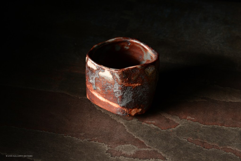 A unique, handcrafted ceramic bowl with a rustic glaze, featuring earthy tones and an irregular shape, resting on a textured surface.
