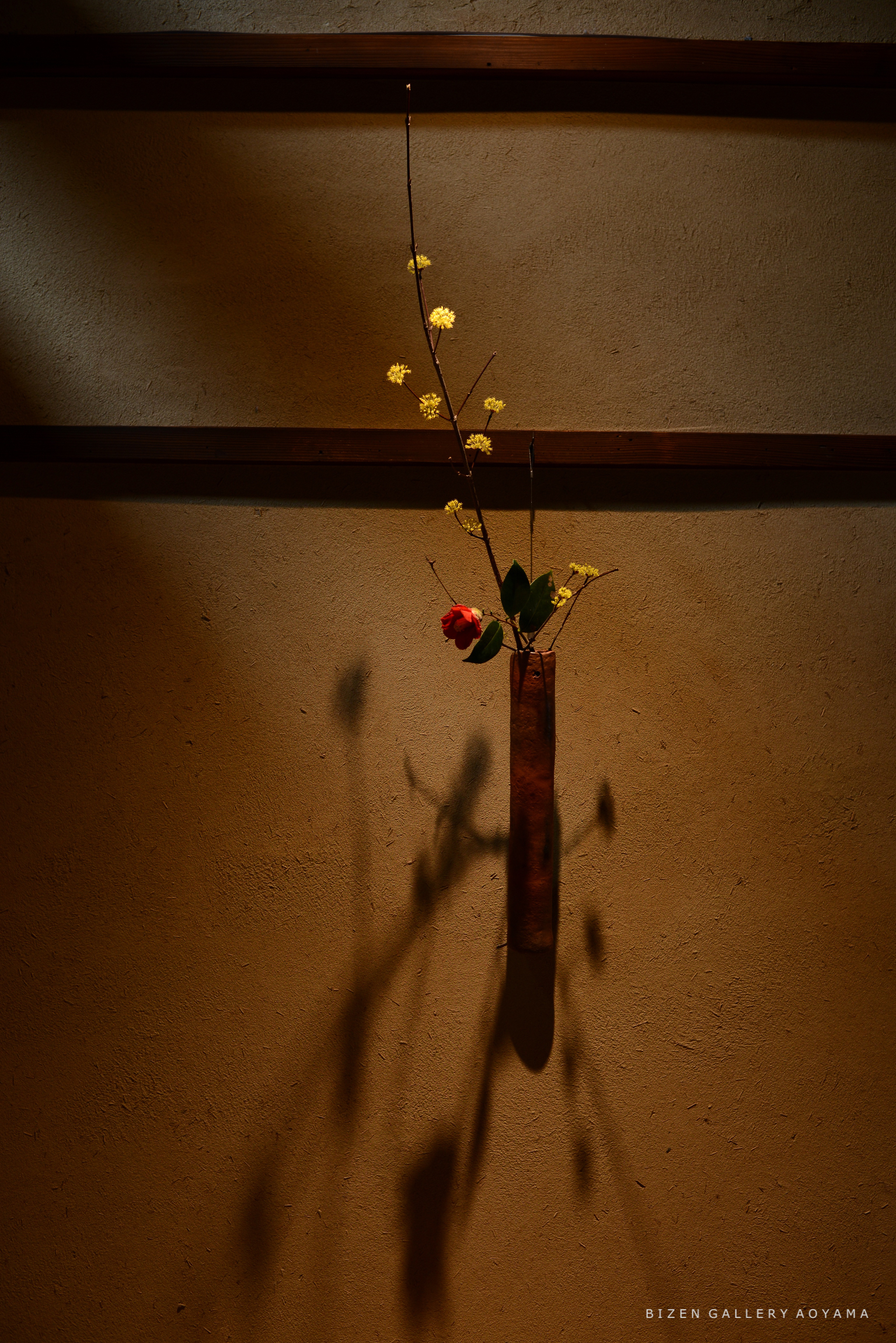 壁に飾られた花瓶に、黄色い花と赤いバラが活けられているシンプルなアート作品