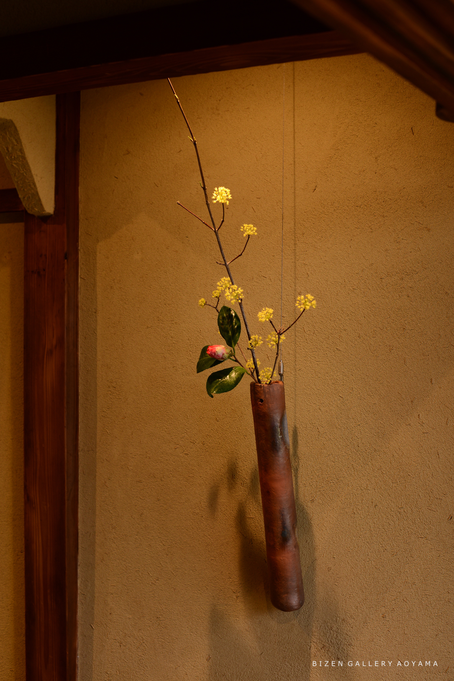 壁に吊るされた花瓶に生けられた黄色い花と緑の葉を持つ枝