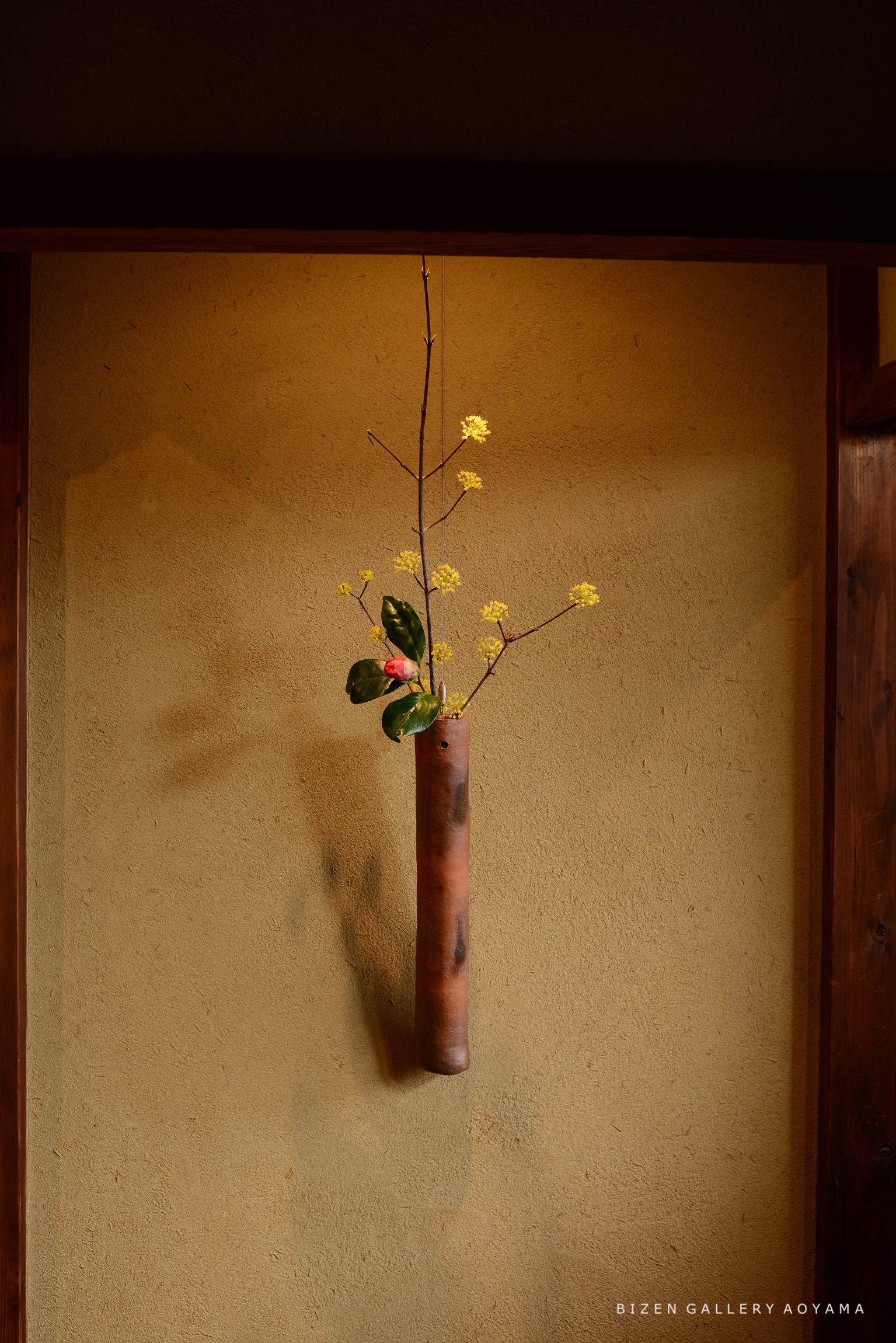 壁に掛けられた陶器の花瓶に活けられた黄色い花と緑の葉