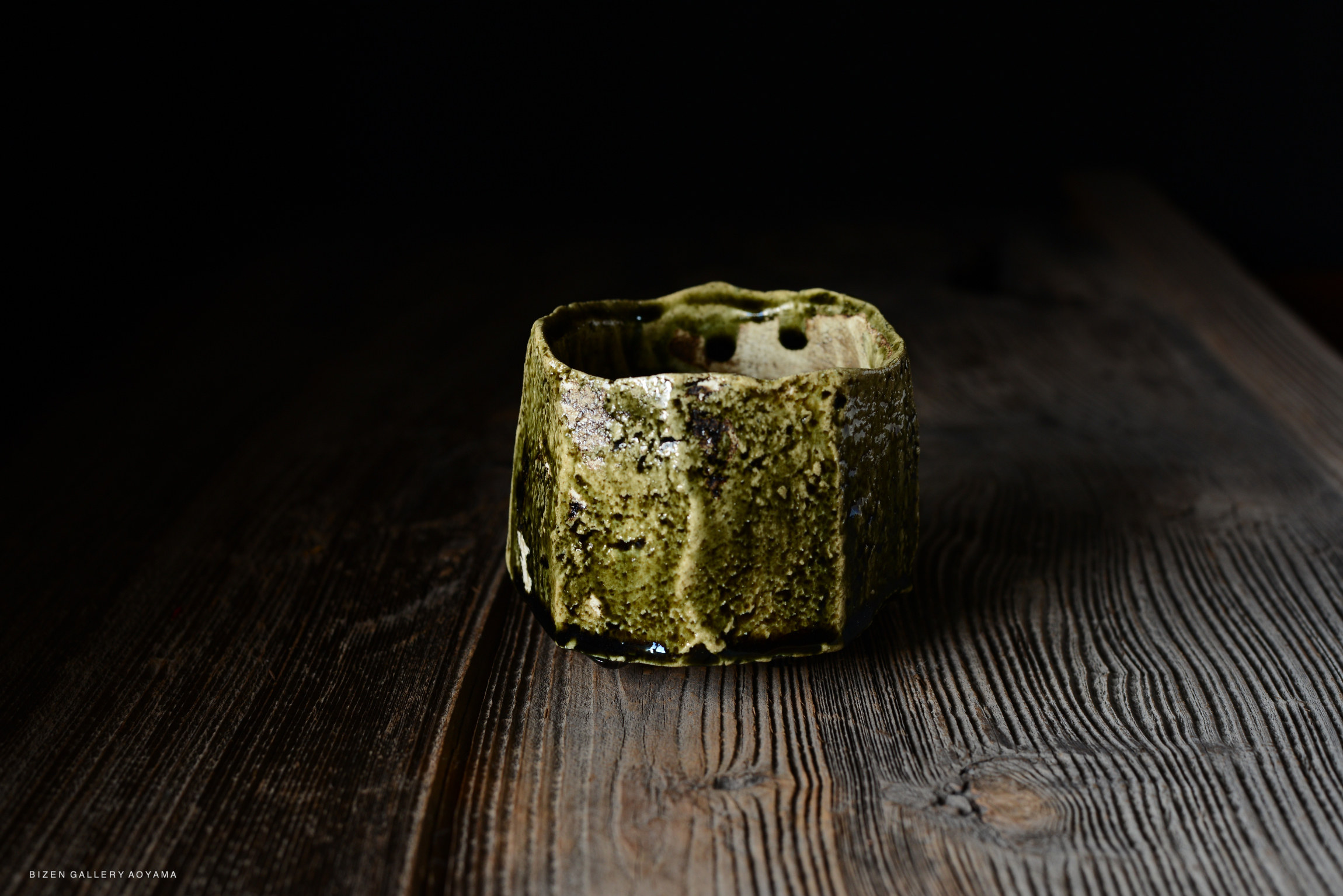 A textured green ceramic vase with a unique shape, placed on a wooden surface.