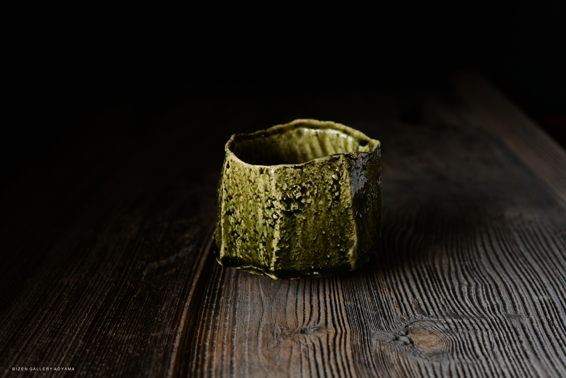 A unique, textured green ceramic cup displayed on a dark wooden surface.