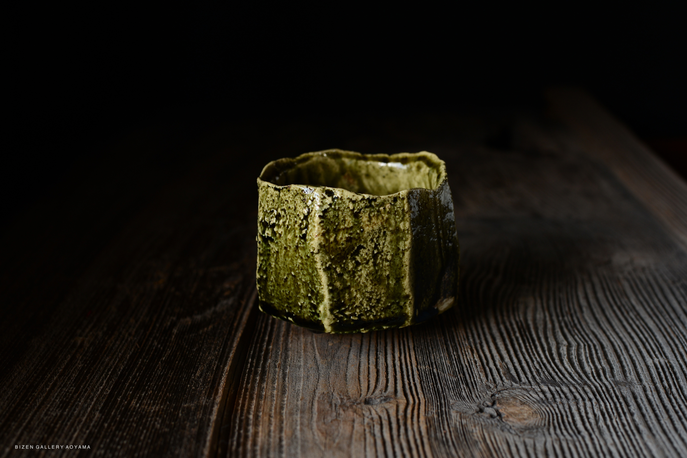 A handcrafted ceramic vessel with a textured green surface, placed on a rustic wooden table.