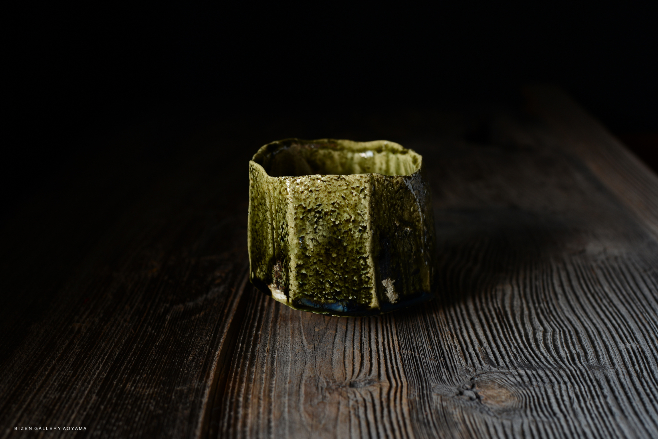 A textured green pottery vessel placed on a wooden table with a dark background.