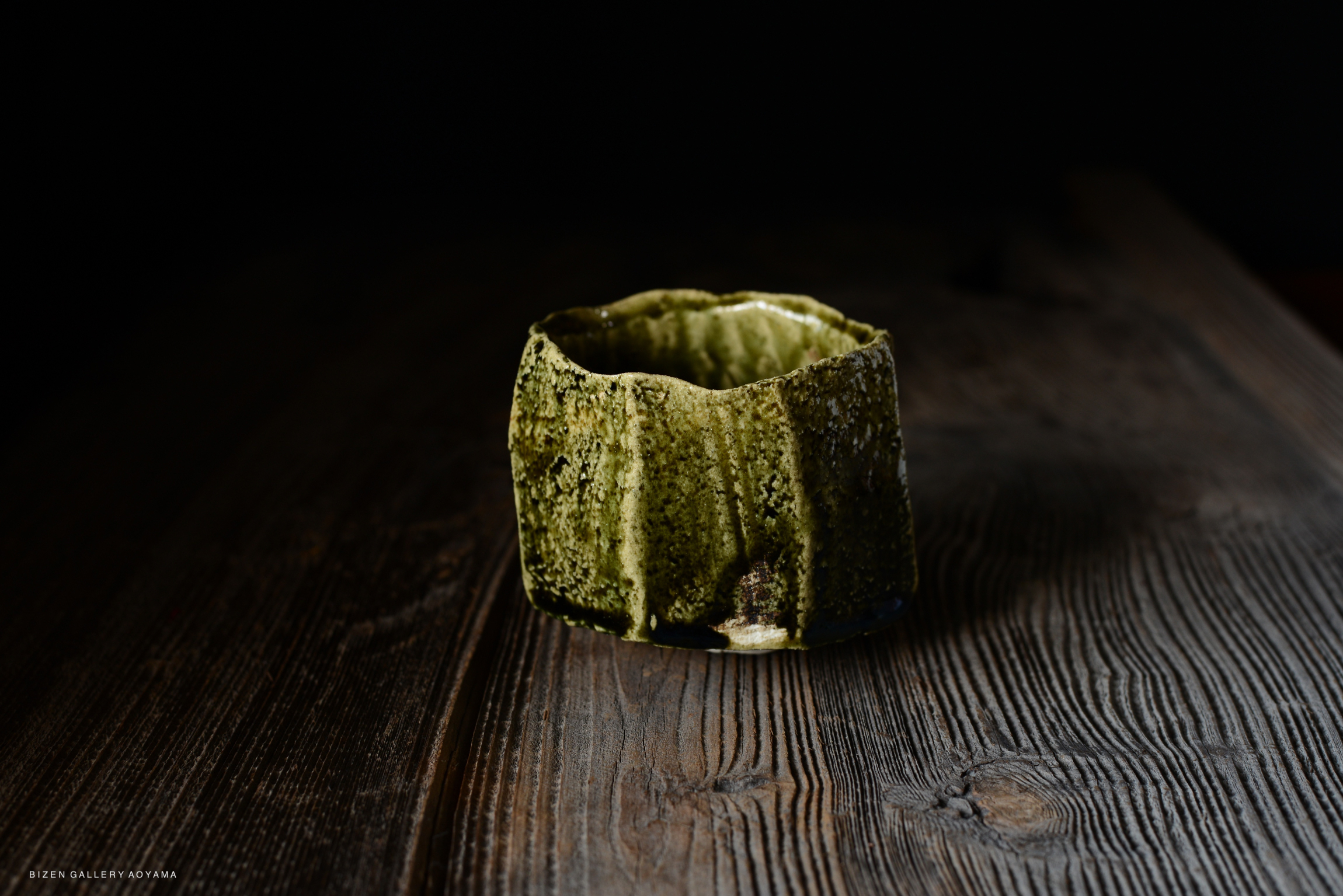 A textured green pottery vessel with a unique, jagged rim, placed on a wooden surface.
