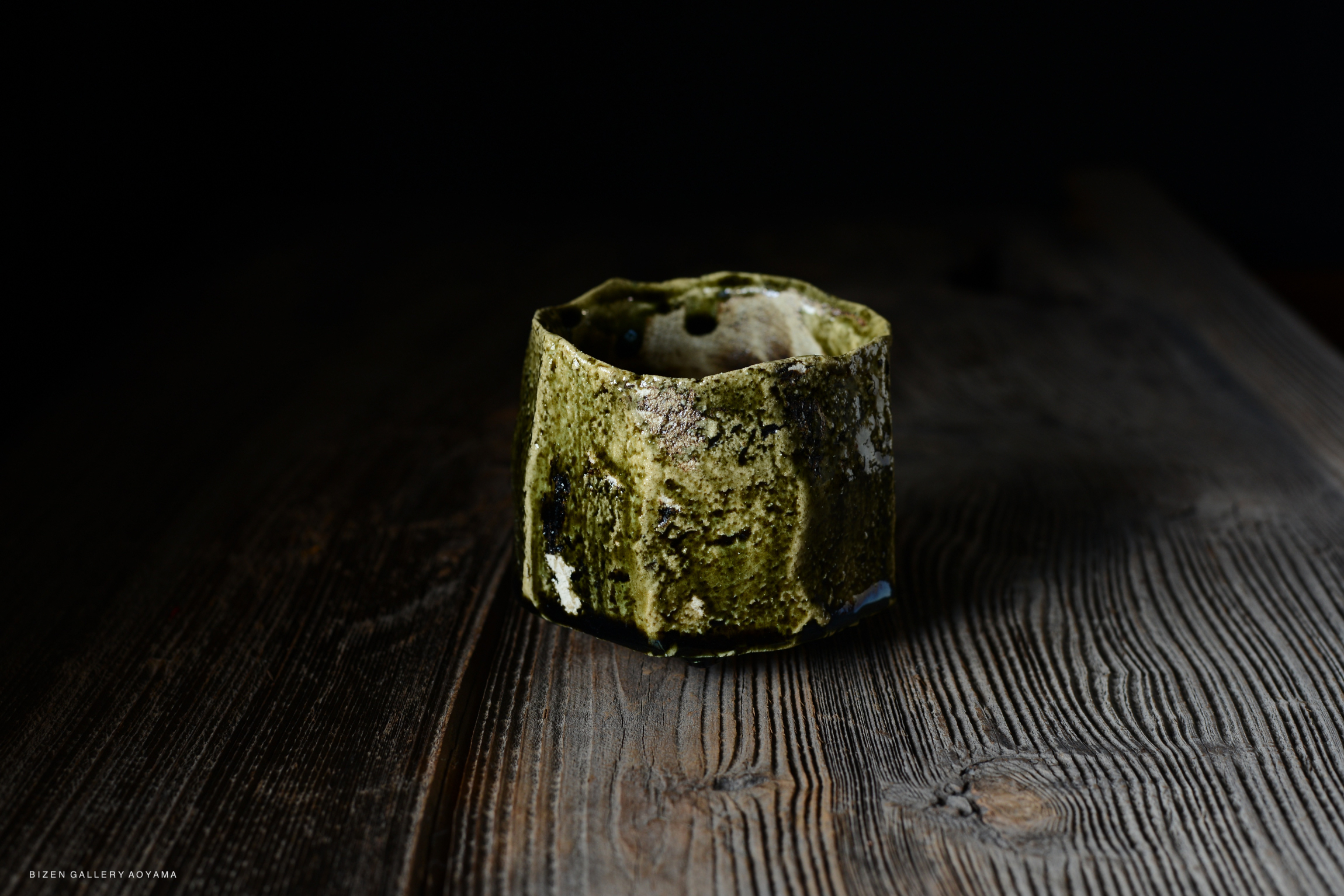 A handcrafted green ceramic cup with a textured surface, placed on a dark wooden table.