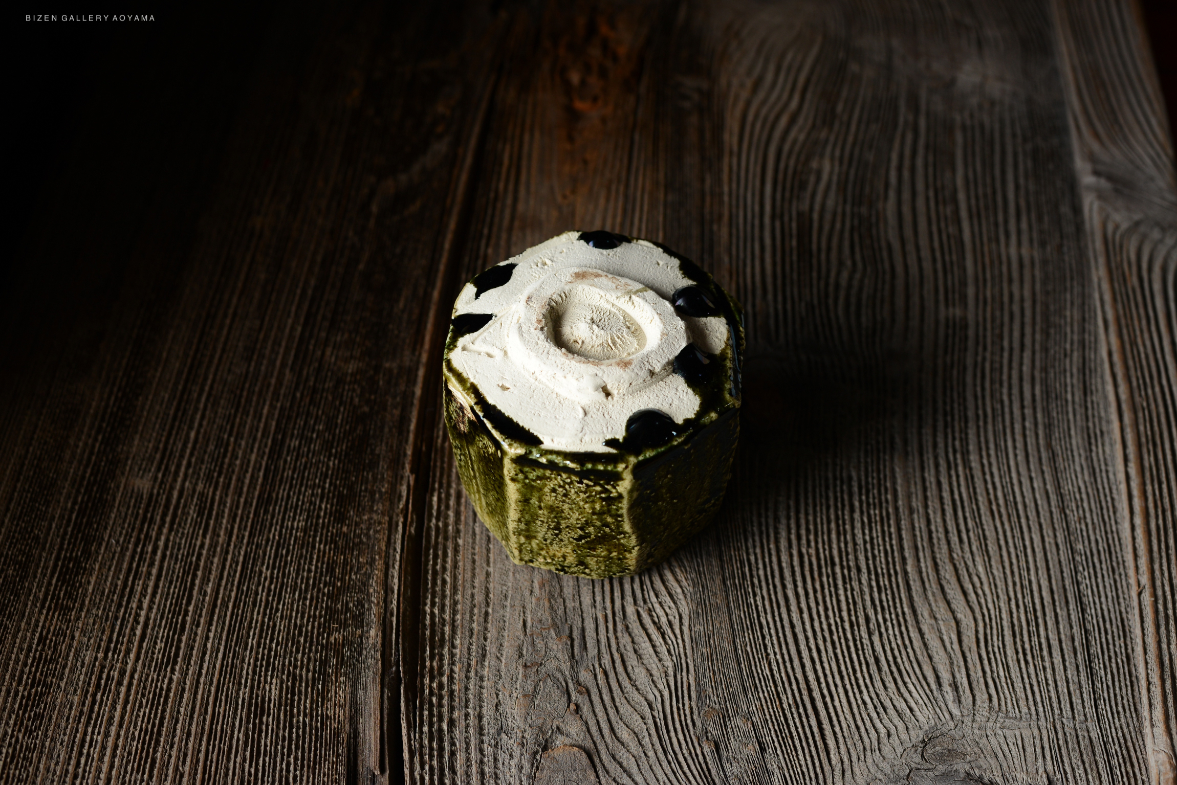 A textured green ceramic pot with a white circular design and black accents on top, placed on a wooden surface.