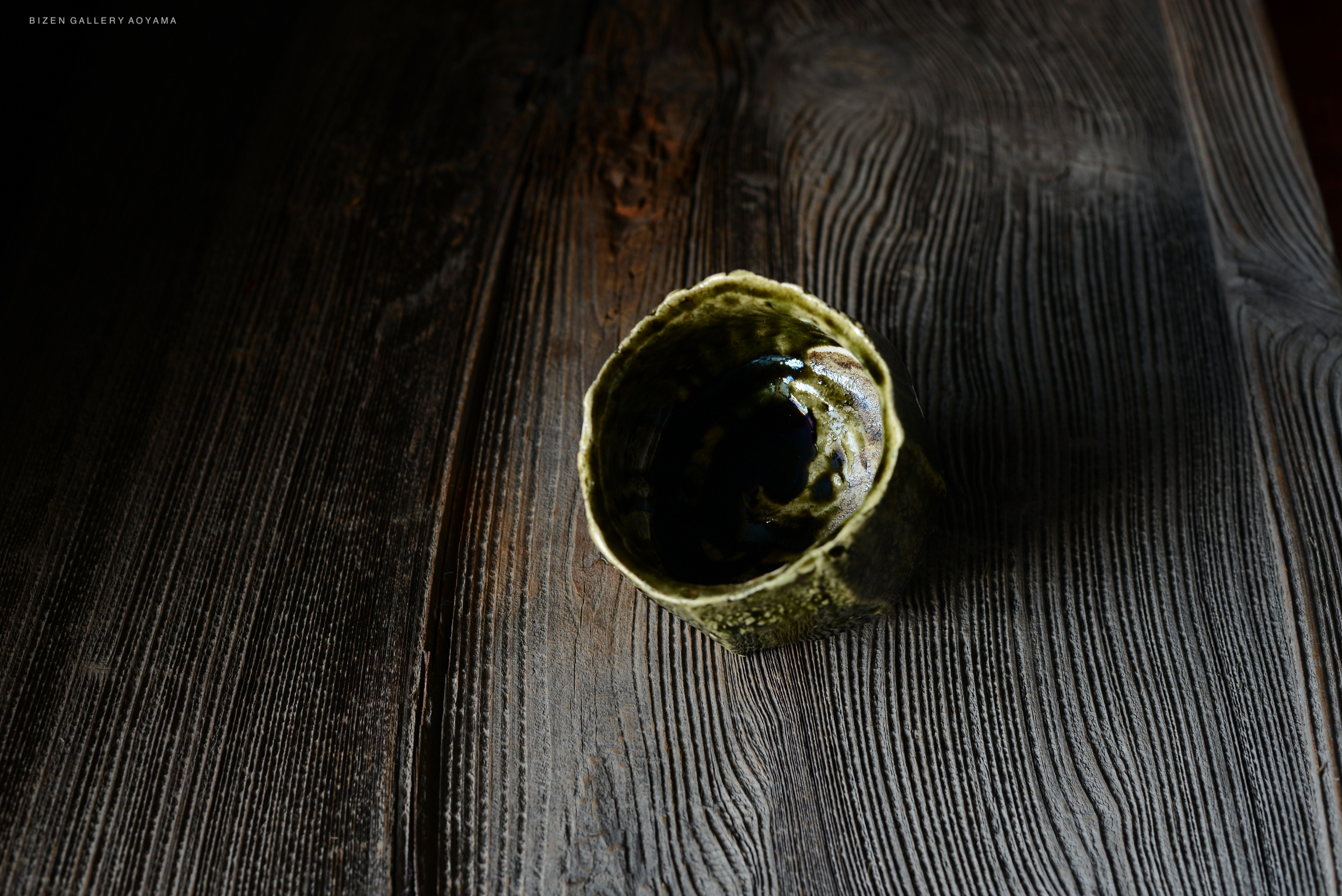 A close-up of a handcrafted ceramic bowl with a textured green exterior, placed on a wooden surface.