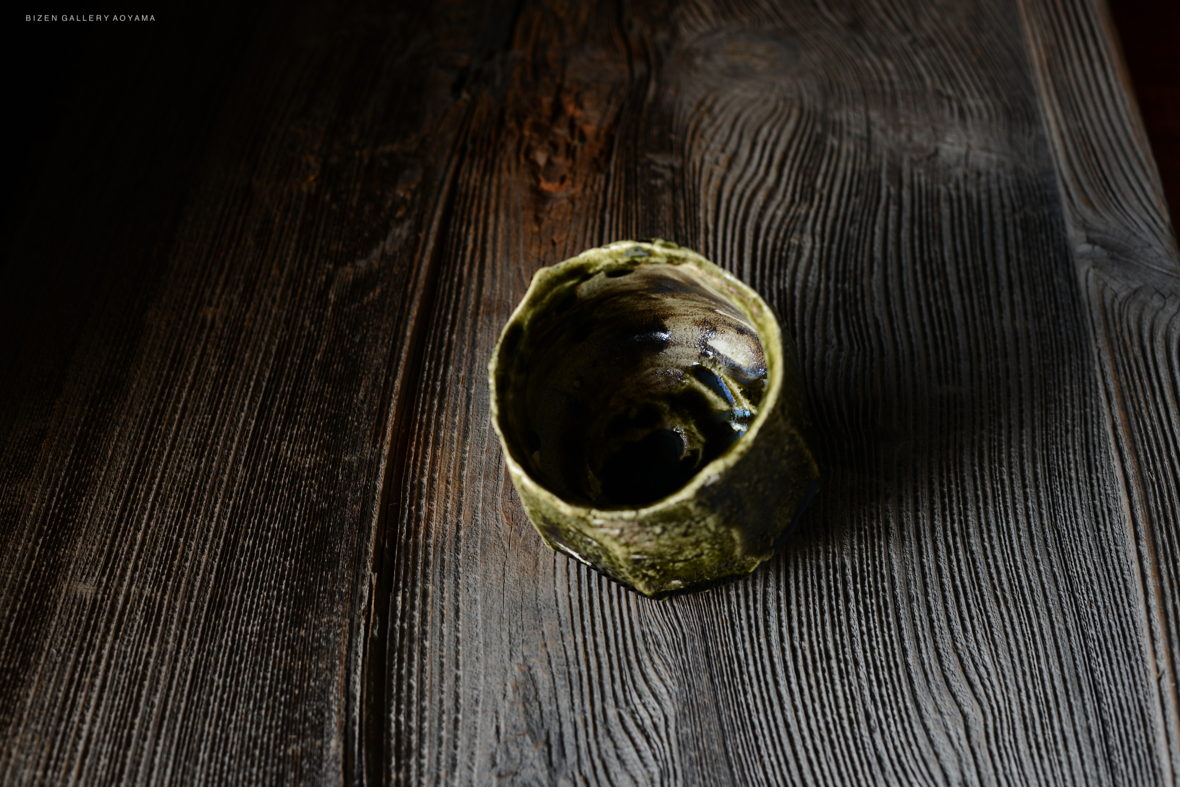 A close-up of a unique ceramic bowl with a textured surface, resting on dark wooden planks.