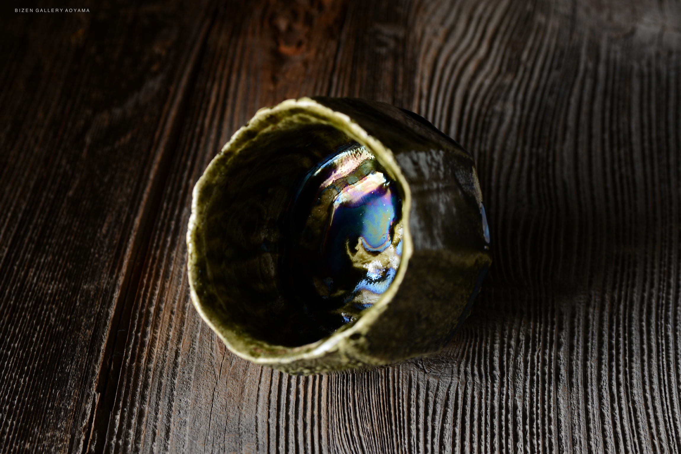 A close-up view of a ceramic bowl with a glossy, iridescent interior, resting on a textured wooden surface.